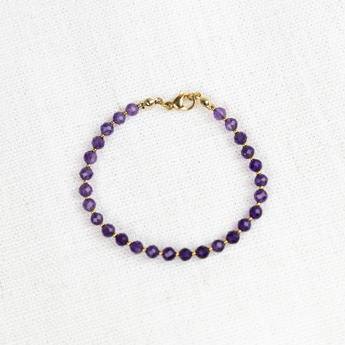 Intuitive Charms Sophia's Glow Amethyst Braided natural Crystal faceted beaded custom Bracelet in gold and purple cord and stainless steel clasp on a light fabric background