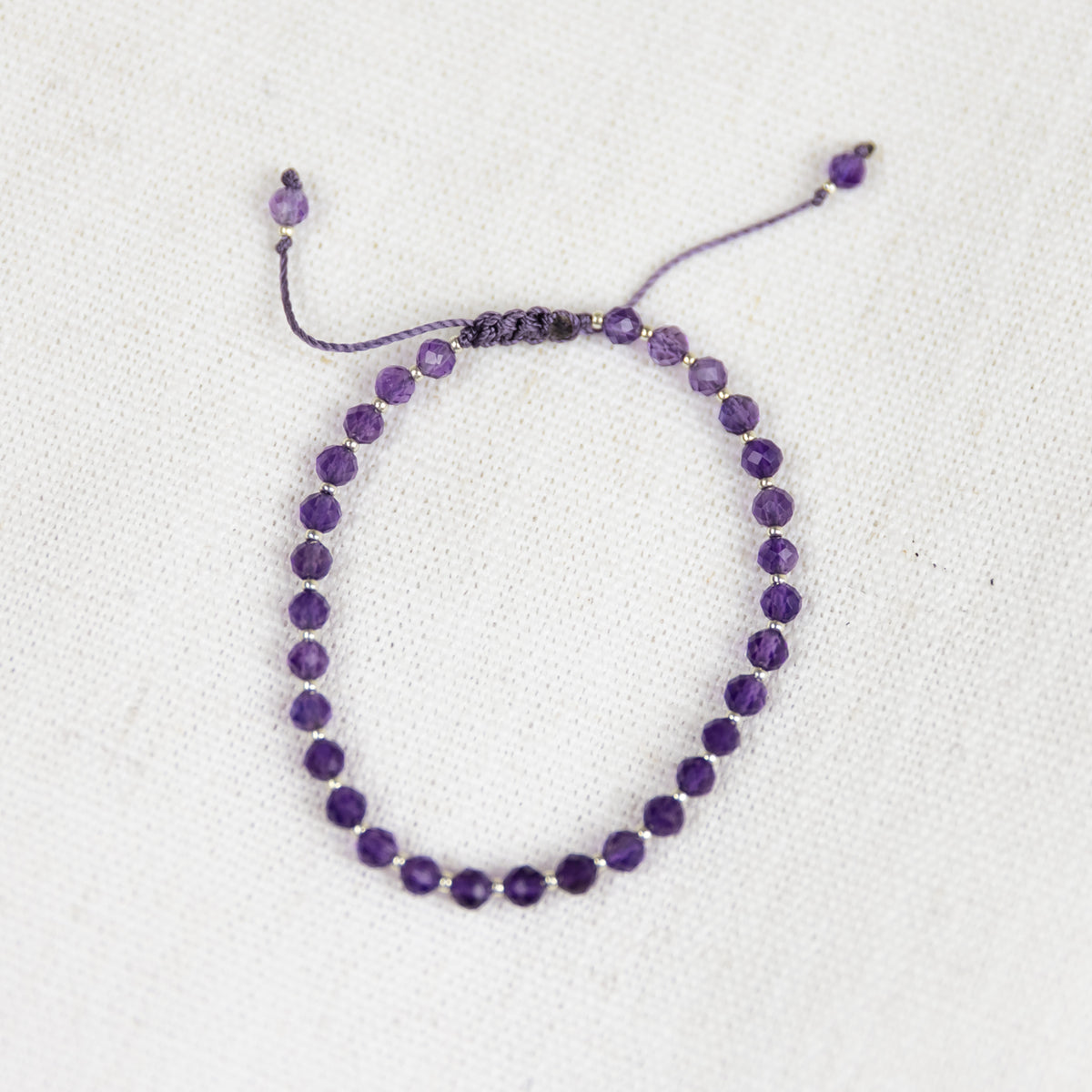 Intuitive Charms Sophia's Glow Amethyst Braided natural Crystal beaded custom Bracelet in silver and purple cord and adjustable clasp extension on a light fabric background