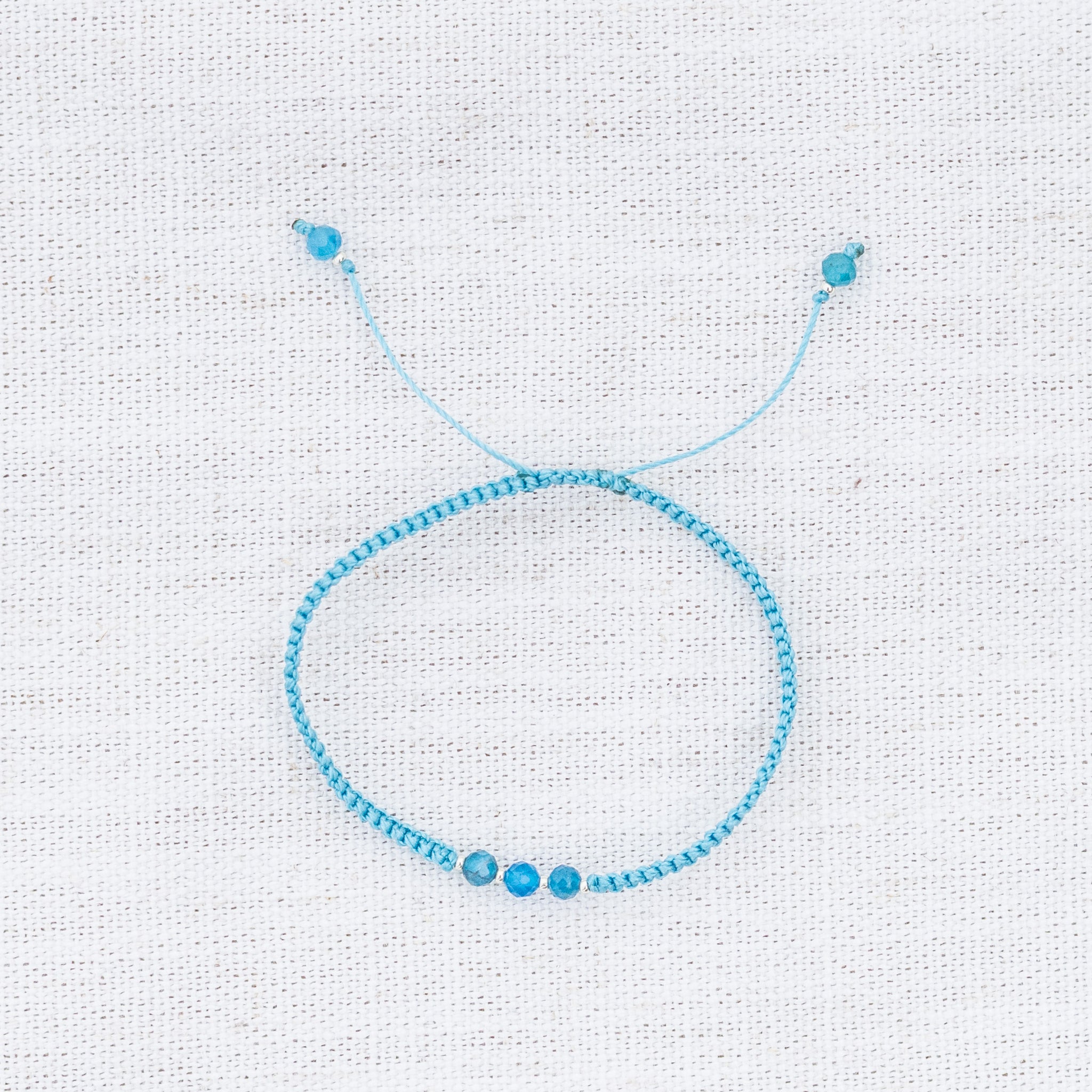 Intuitive Charms Delphina's Guard Apatite Braided natural Crystal beaded custom Bracelet in silver and blue cord on a light fabric background