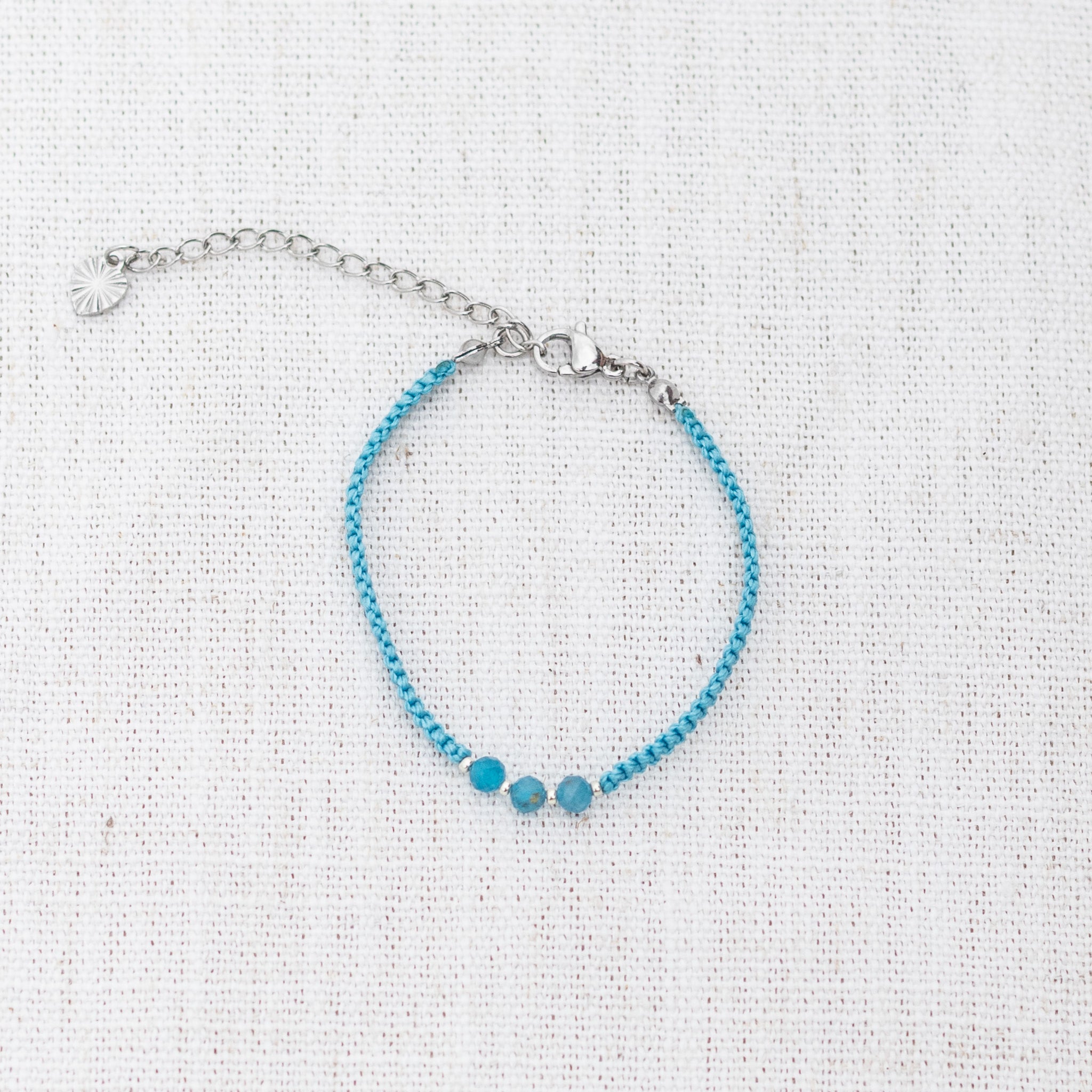 Intuitive Charms Delphina's Guard Apatite Braided natural Crystal beaded custom Bracelet in silver and blue cord and clasp extension on a light fabric background