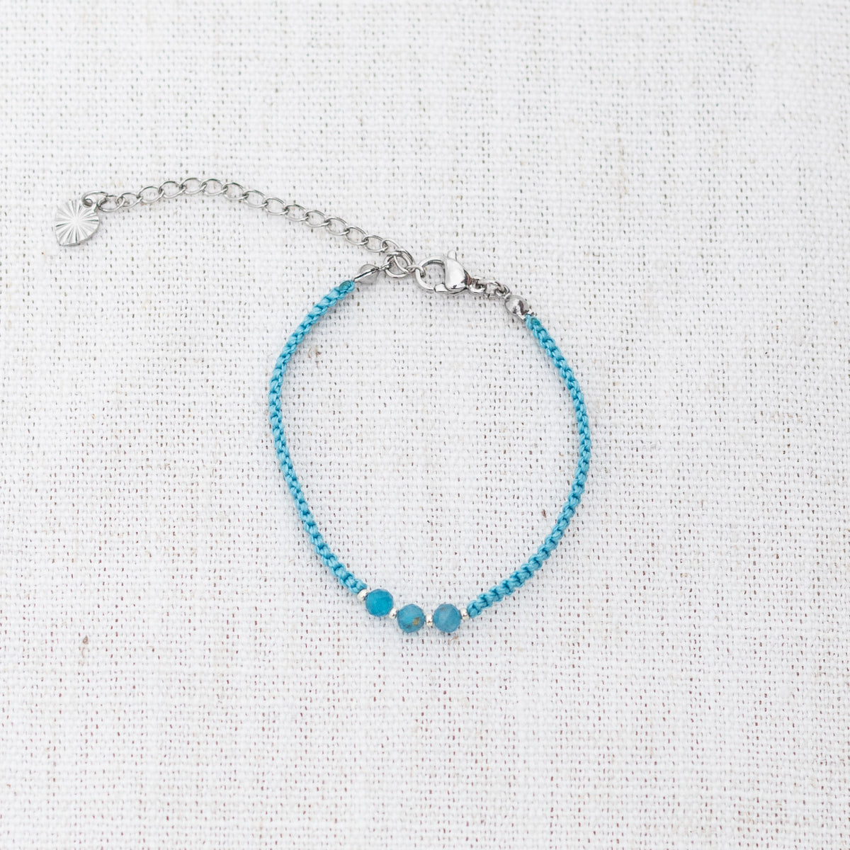 Intuitive Charms Delphina's Guard Apatite Braided natural Crystal beaded custom Bracelet in silver and blue cord and clasp extension on a light fabric background