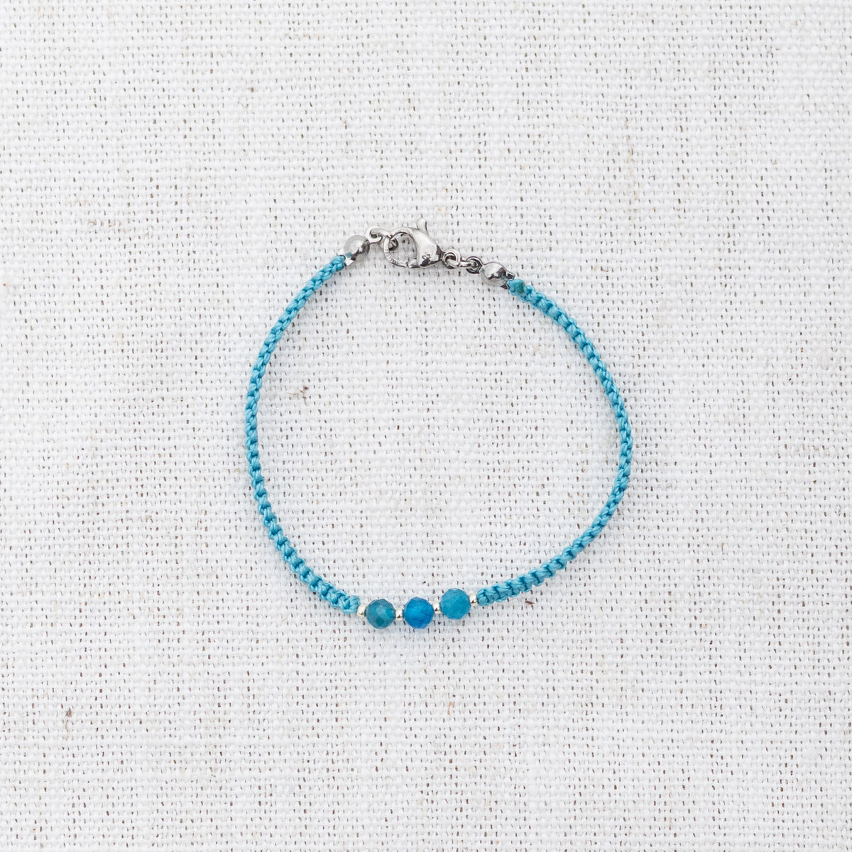 Intuitive Charms Delphina's Guard Apatite Braided natural Crystal beaded custom Bracelet in silver and blue cord and clasp on a light fabric background