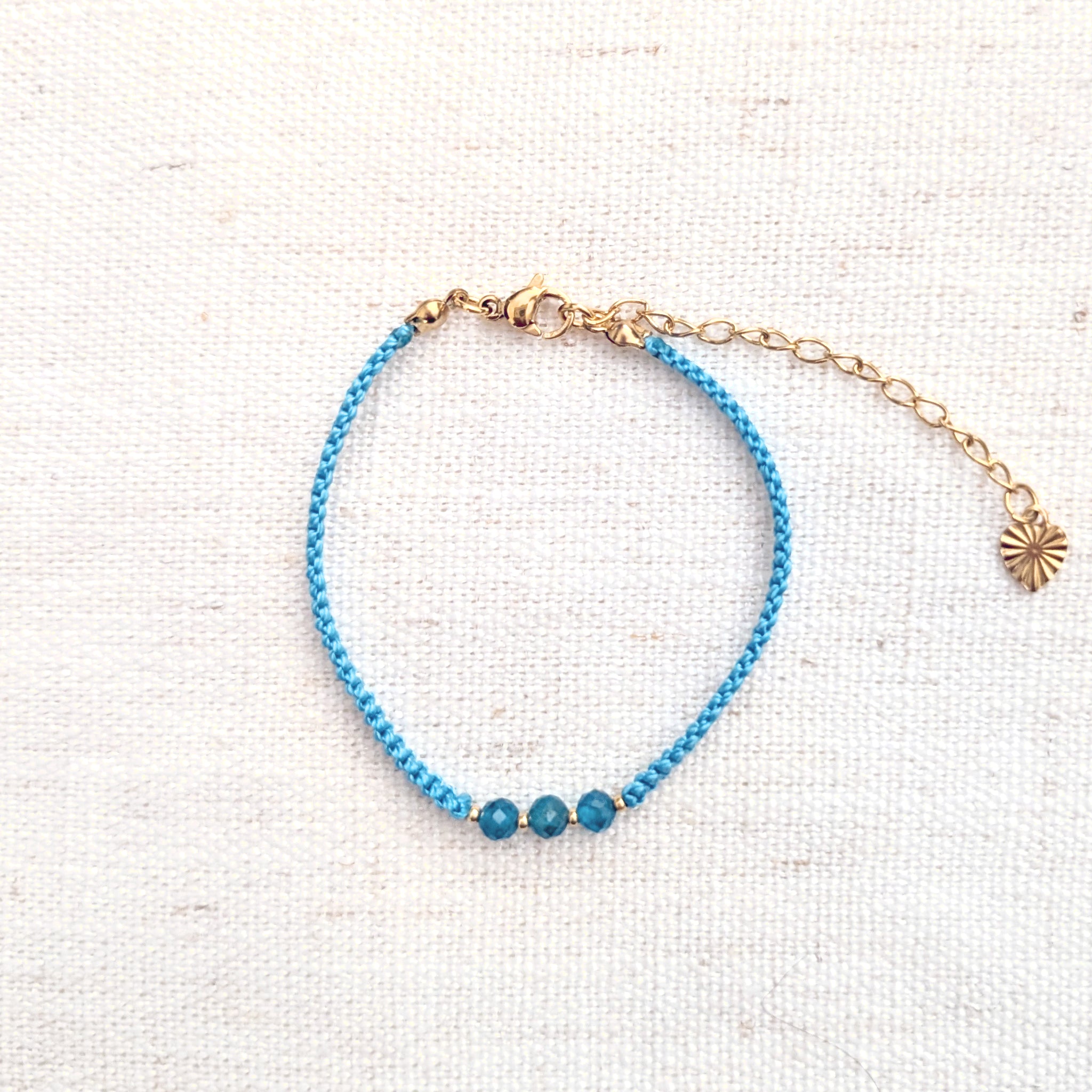 Intuitive Charms Delphina's Guard Apatite Braided natural Crystal beaded custom Bracelet in gold and blue cord and clasp extension on a light fabric background
