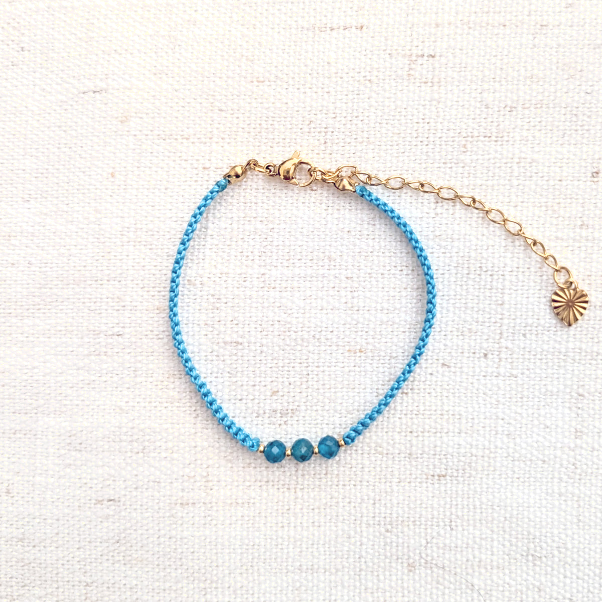 Intuitive Charms Delphina's Guard Apatite Braided natural Crystal beaded custom Bracelet in gold and blue cord and clasp extension on a light fabric background
