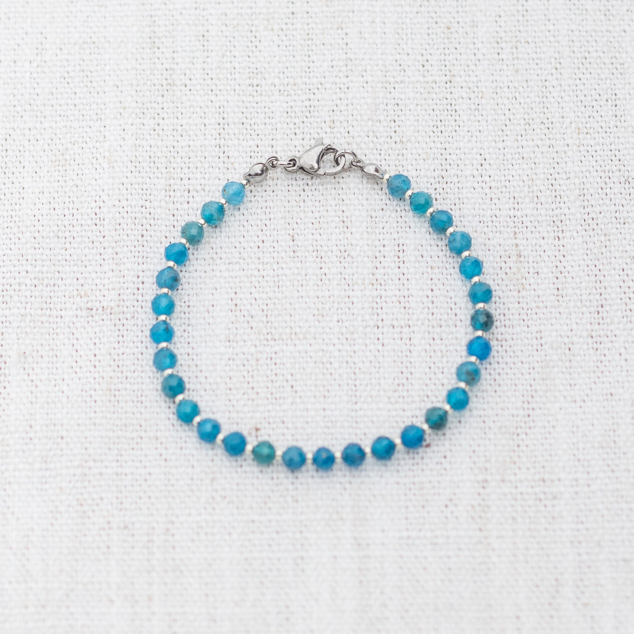 Intuitive Charms Delphina's Glow Apatite Braided natural Crystal beaded custom Bracelet in silver and blue cord and clasp on a light fabric background