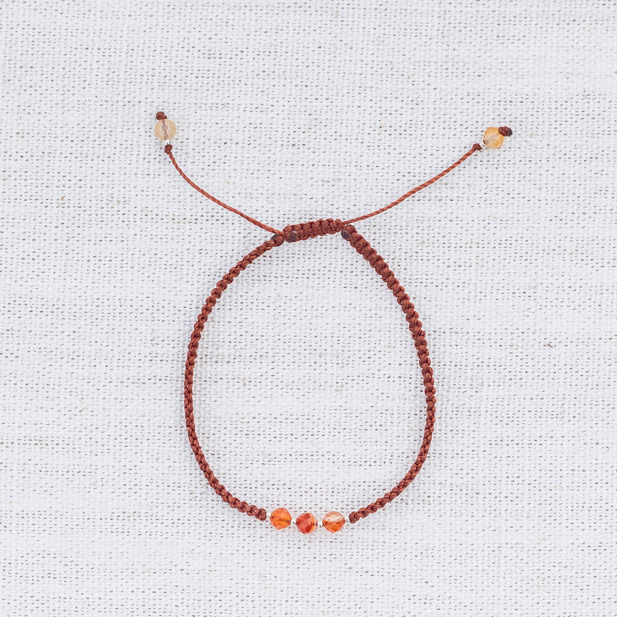 Intuitive Charms Coralia's Guard Carnelian Braided natural Crystal beaded custom Bracelet in silver and red cord on light fabric background