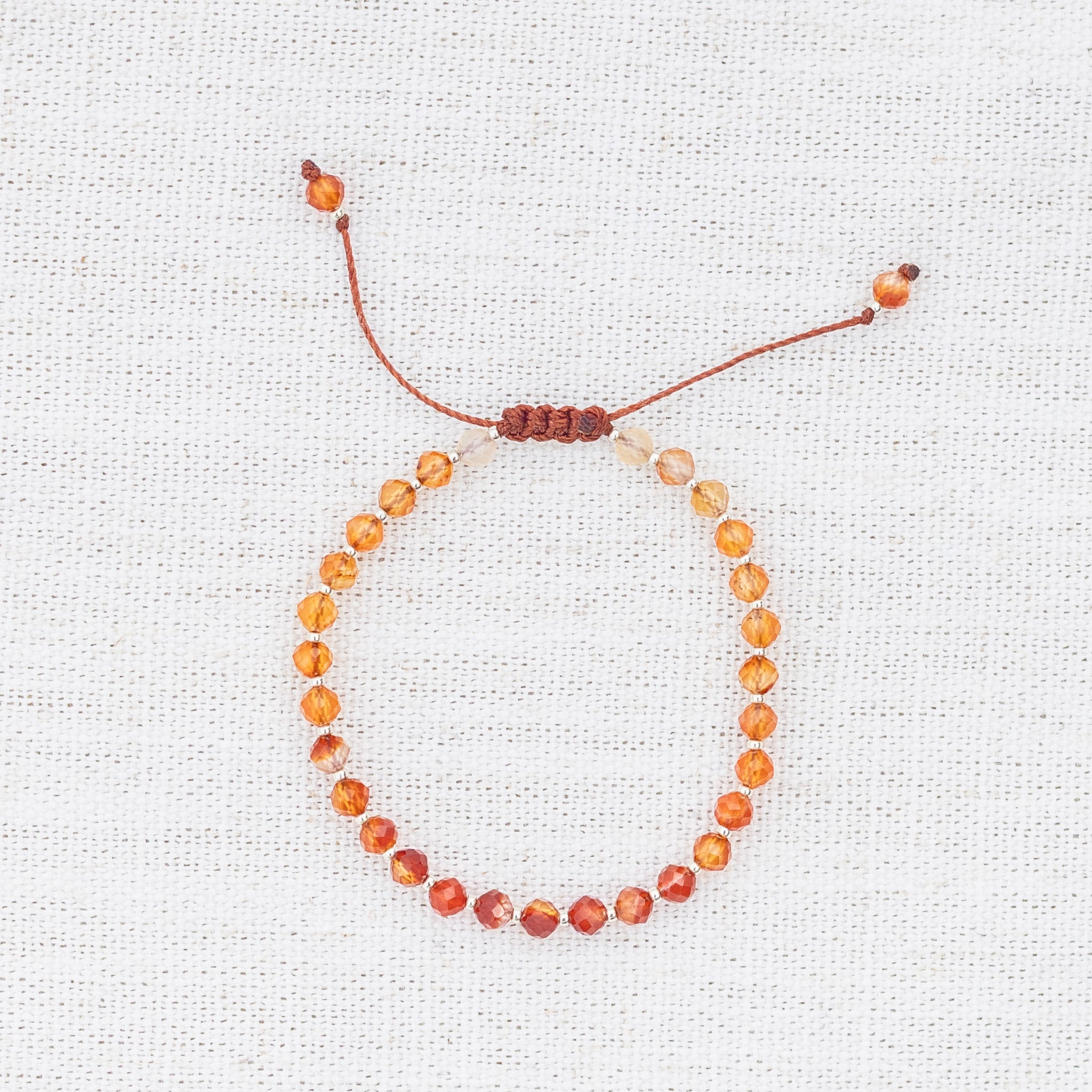 Intuitive Charms Coralia's Glow Carnelian Braided natural Crystal beaded custom Bracelet in silver and red cord on light fabric background