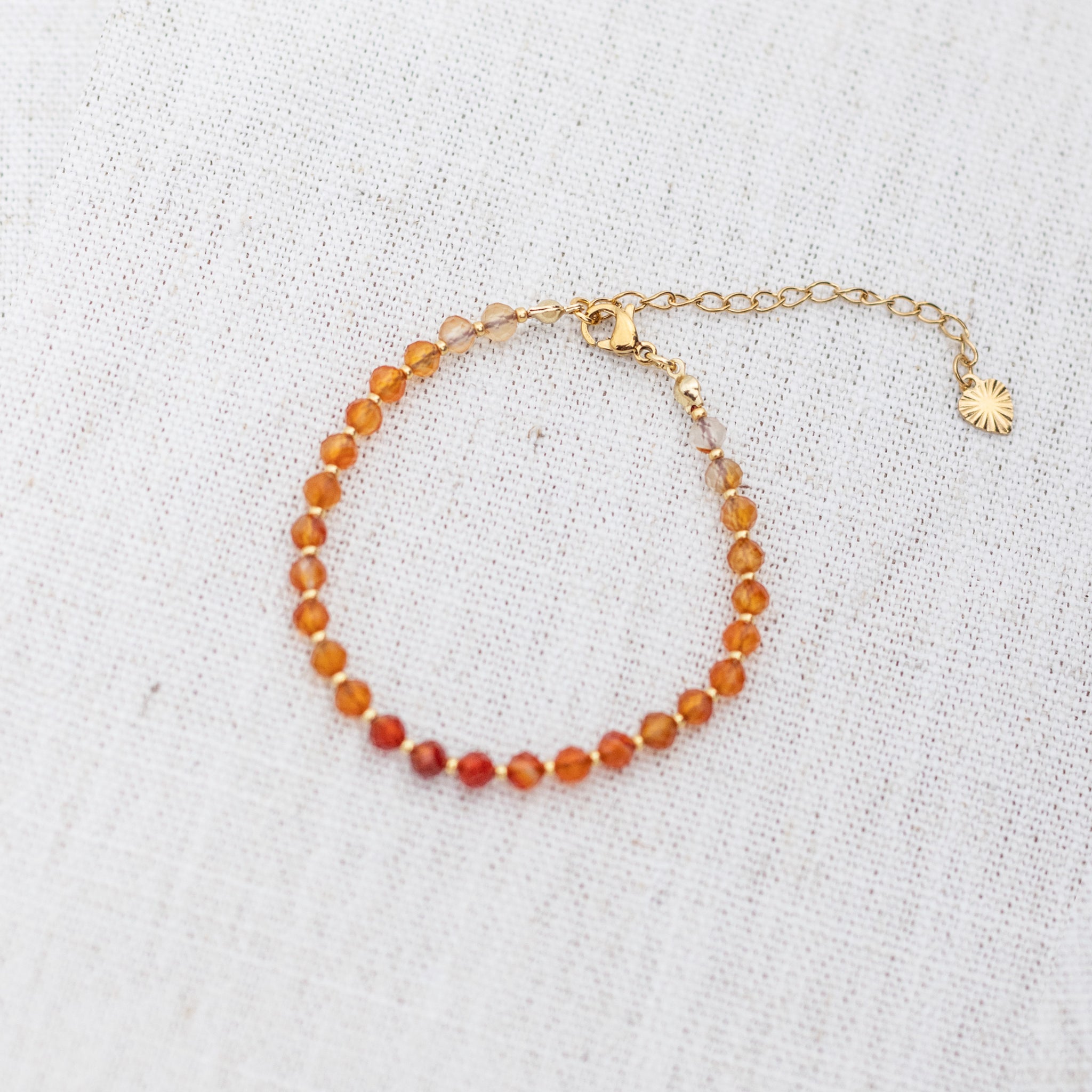 Intuitive Charms Coralia's Glow Carnelian Braided natural Crystal beaded custom Bracelet in gold and red cord and clasp extension on a light fabric background