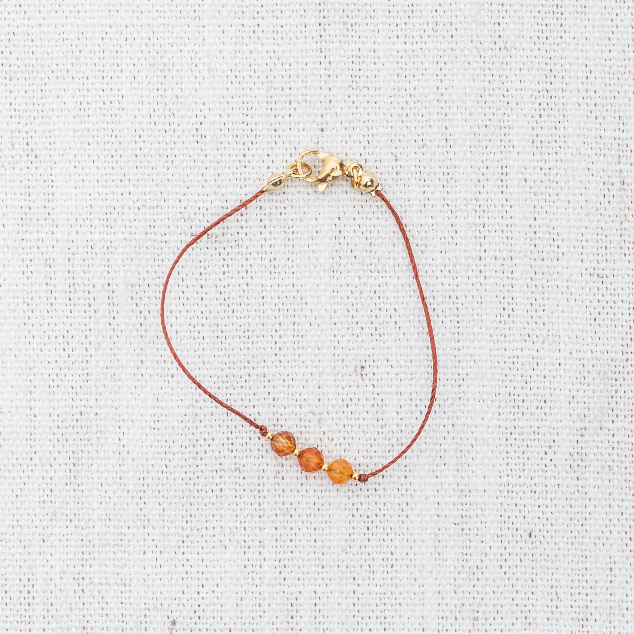 Intuitive Charms Coralia's Mist Carnelian Braided natural Crystal beaded custom Bracelet in gold and red cord and clasp on light fabric background