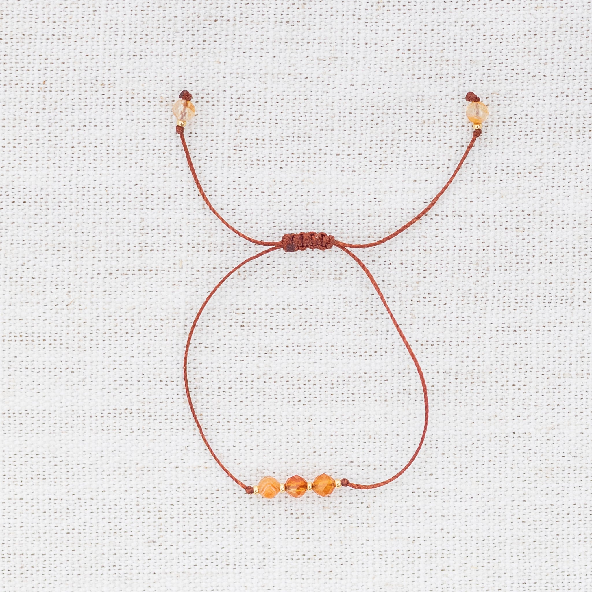 Intuitive Charms Coralia's Mist Carnelian Braided natural Crystal beaded custom Bracelet in gold and red cord on light fabric background