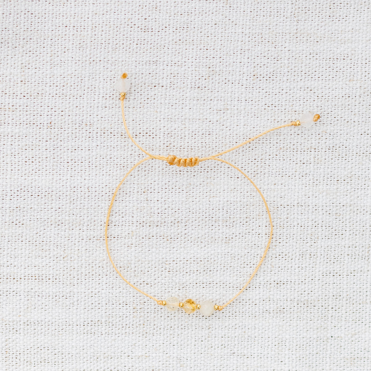 Intuitive Charms Eos's Mist Citrine Braided natural Crystal beaded custom Bracelet in gold and yellow cord on a light fabric background