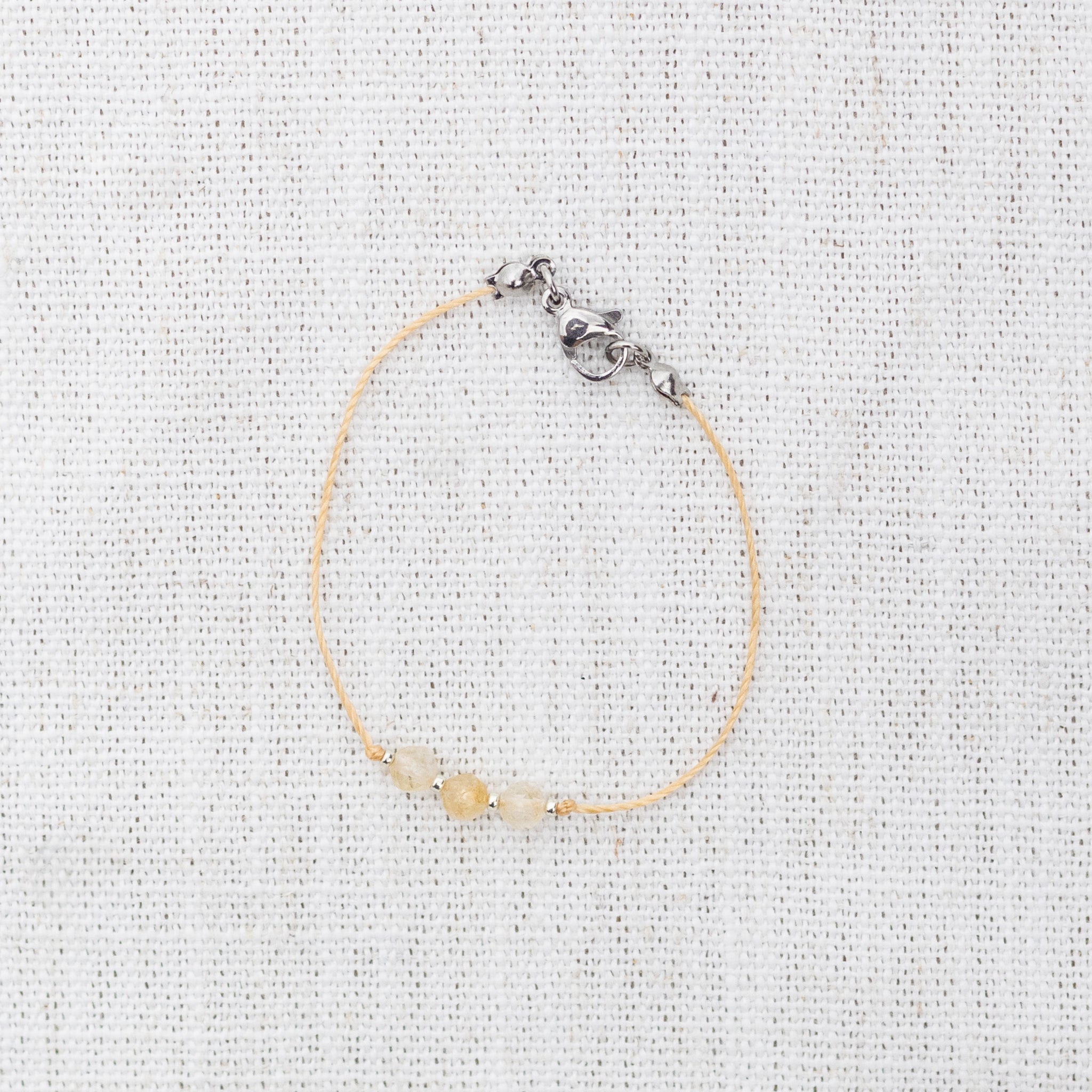 Intuitive Charms Eos's Mist Citrine Braided natural Crystal beaded custom Bracelet in silver and yellow cord and clasp on a light fabric background