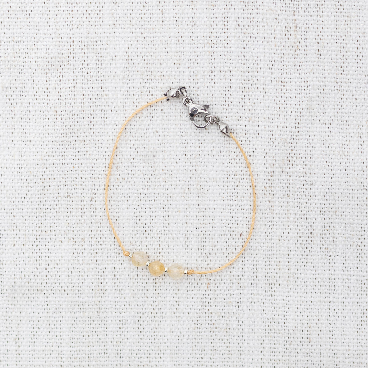 Intuitive Charms Eos's Mist Citrine Braided natural Crystal beaded custom Bracelet in silver and yellow cord and clasp on a light fabric background