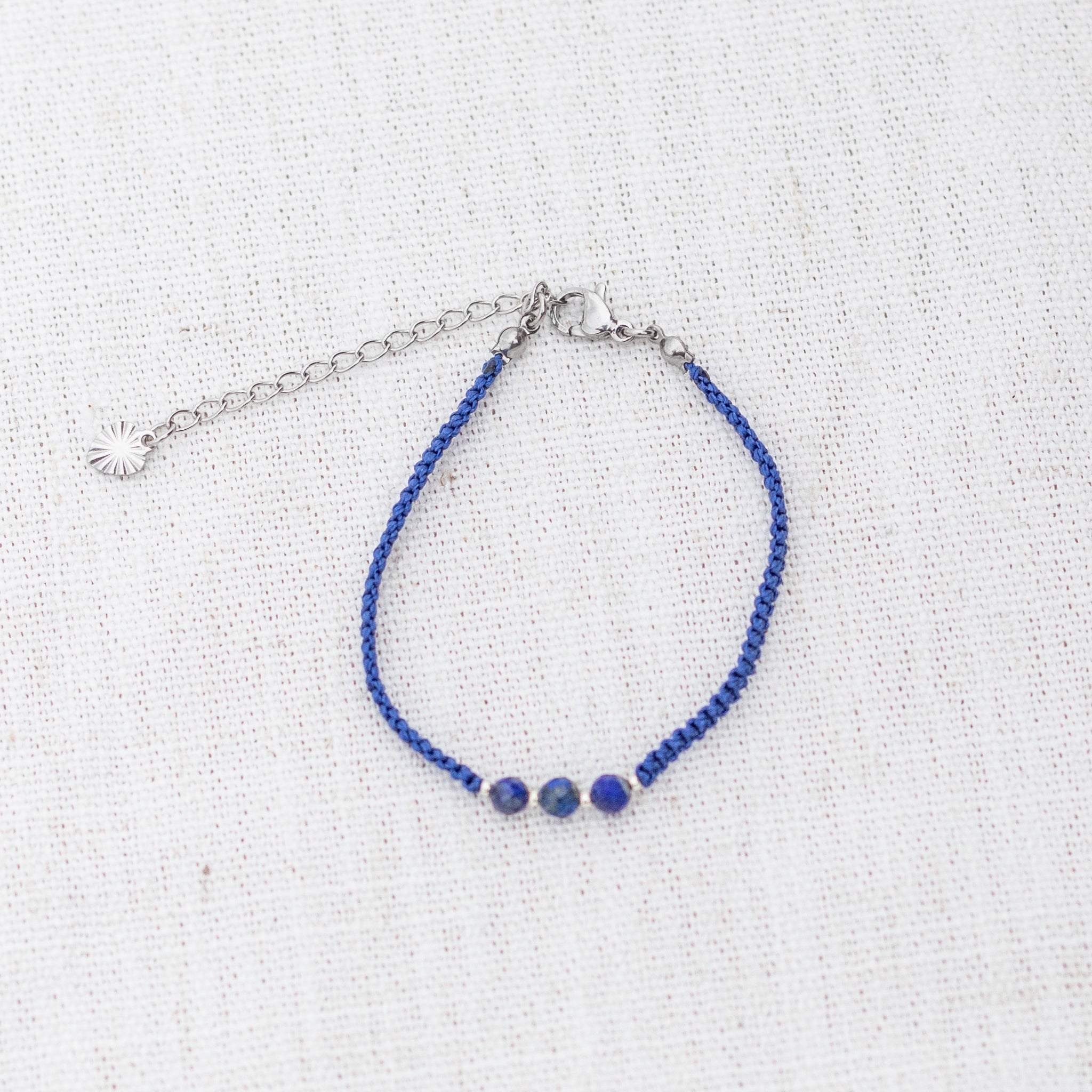 Intuitive Charms Amphitrite's Guard Lapis Lazuli Braided natural Crystal beaded custom Bracelet in silver and deep blue cord and clasp extension on a light fabric background