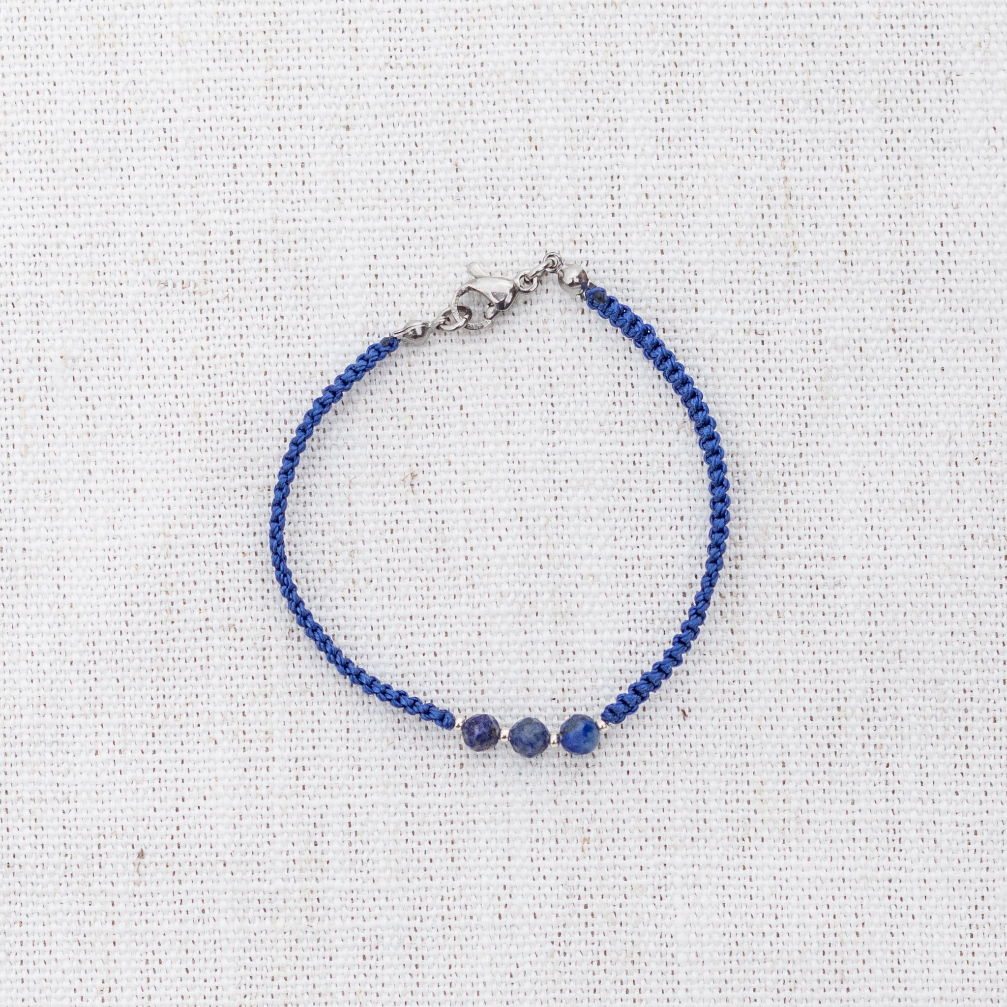 Intuitive Charms Amphitrite's Guard Lapis Lazuli Braided natural Crystal beaded custom Bracelet in silver and deep blue cord and clasp on a light fabric background
