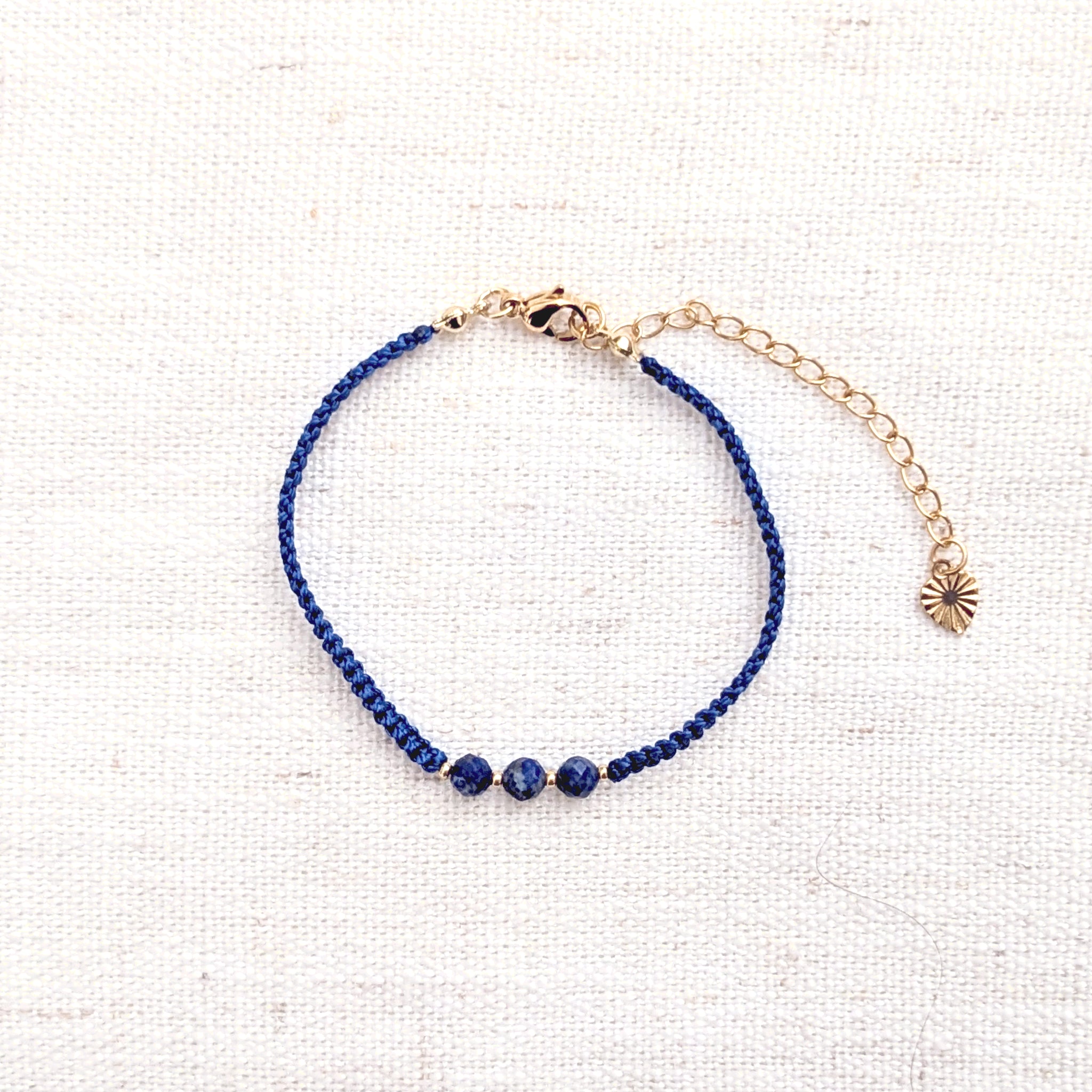 Intuitive Charms Amphitrite's Guard Lapis Lazuli Braided natural Crystal beaded custom Bracelet in gold and deep blue cord and clasp extension on a light fabric background