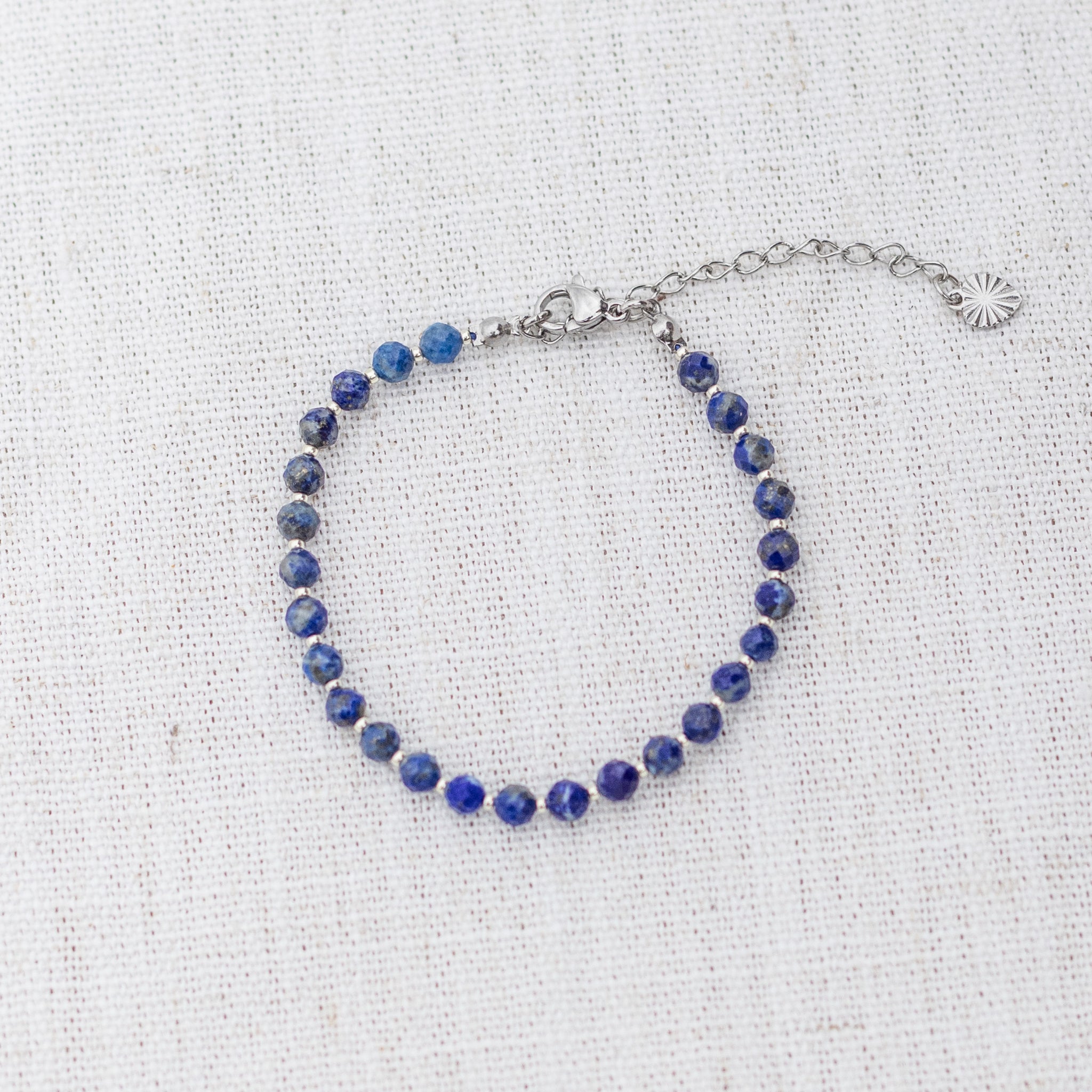Intuitive Charms Amphitrite's Glow Lapis Lazuli Braided natural Crystal beaded custom Bracelet in silver and deep blue cord and clasp extension on a light fabric background