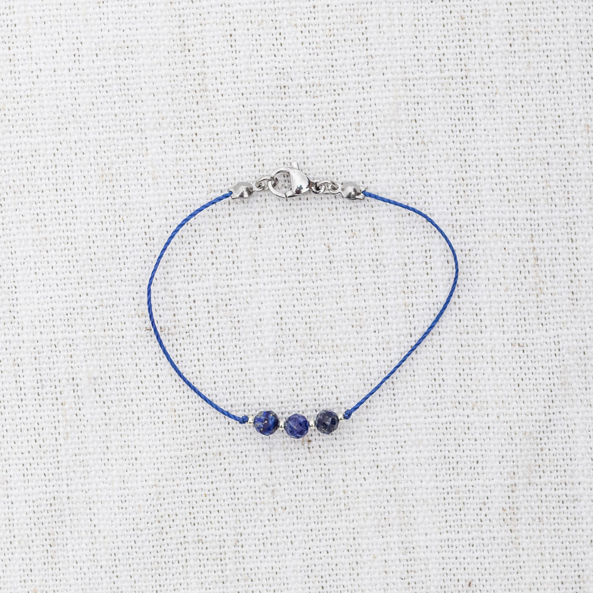 Intuitive Charms Amphitrite's Mist Lapis Lazuli Braided natural Crystal beaded custom Bracelet in silver and deep blue cord and clasp on a light fabric background
