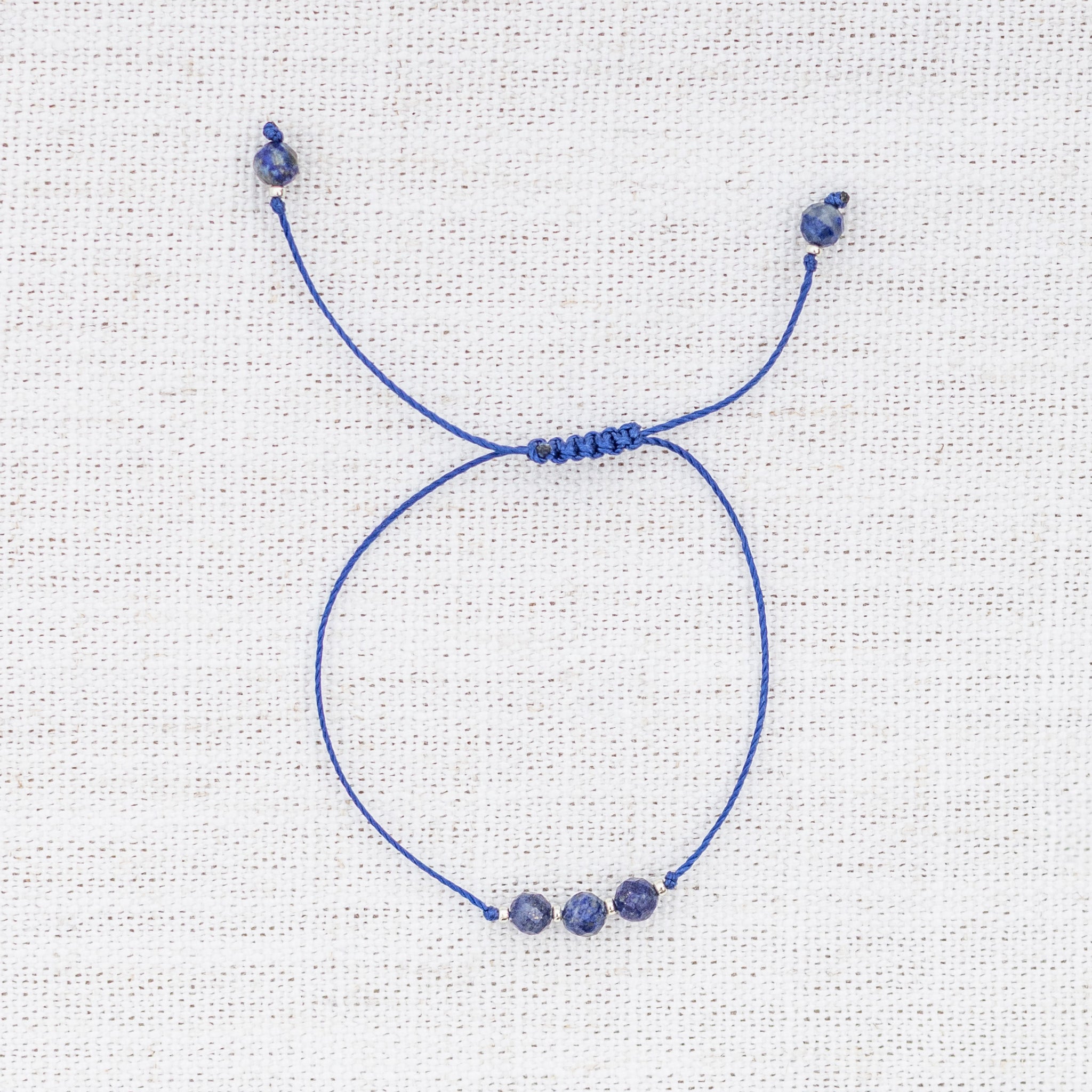 Intuitive Charms Amphitrite's Mist Lapis Lazuli Braided natural Crystal beaded custom Bracelet in silver and deep blue cord on a light fabric background
