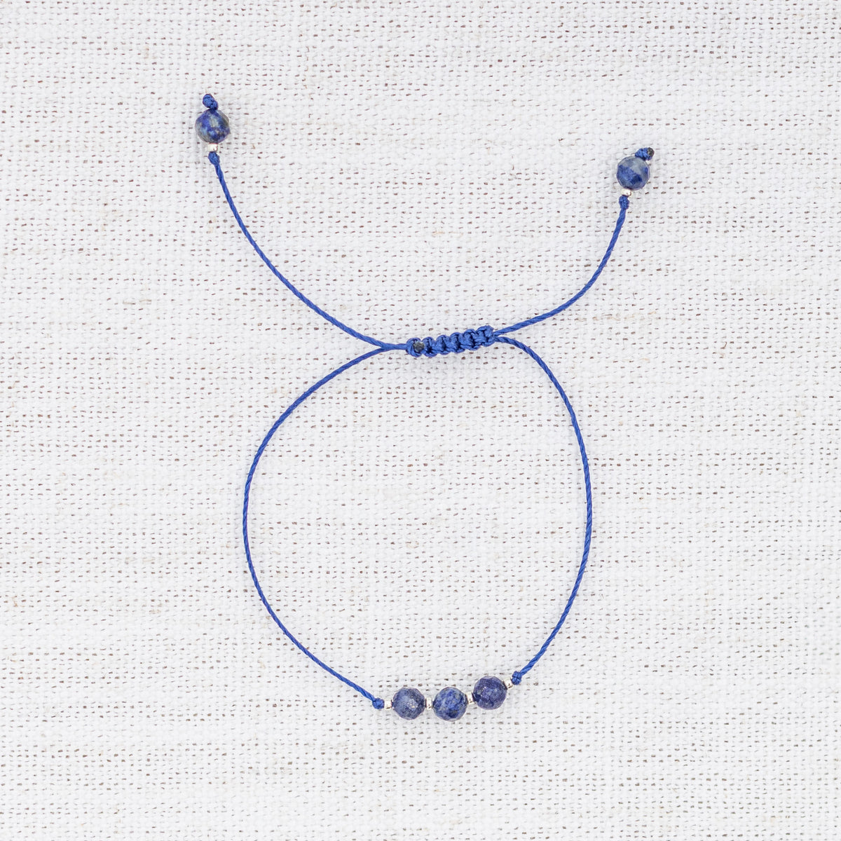 Intuitive Charms Amphitrite's Mist Lapis Lazuli Braided natural Crystal beaded custom Bracelet in silver and deep blue cord on a light fabric background