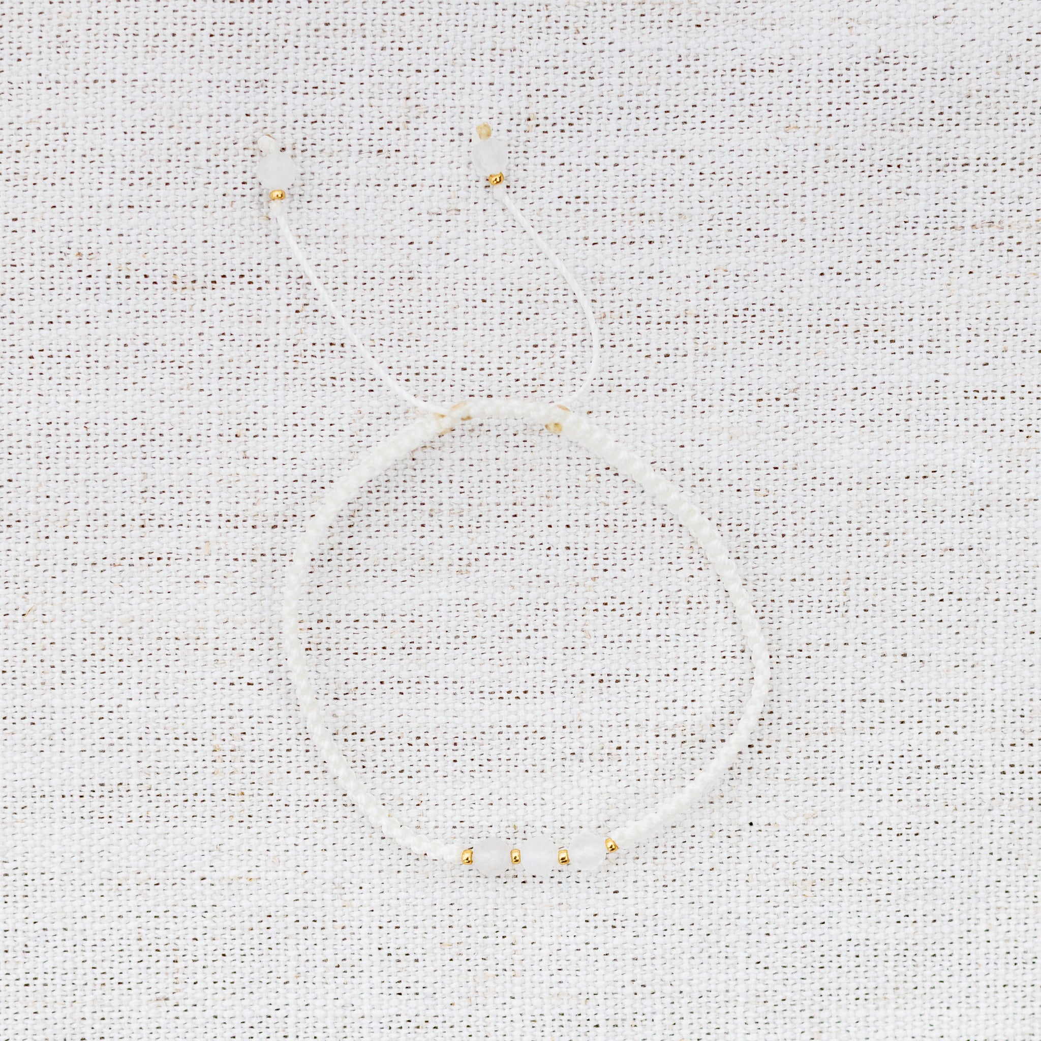 Intuitive Charms Selene's Guard Moonstone Braided natural Crystal beaded custom Bracelet in gold and white cord on a light fabric background