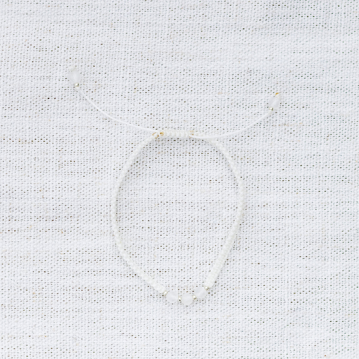 Intuitive Charms Selene's Guard Moonstone Braided natural Crystal beaded custom Bracelet in silver and white cord on a light fabric background