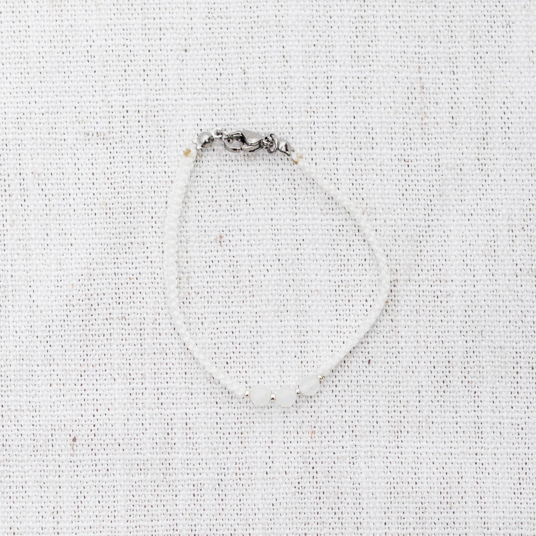 Intuitive Charms Selene's Guard Moonstone Braided natural Crystal beaded custom Bracelet in silver and white cord and clasp on a light fabric background