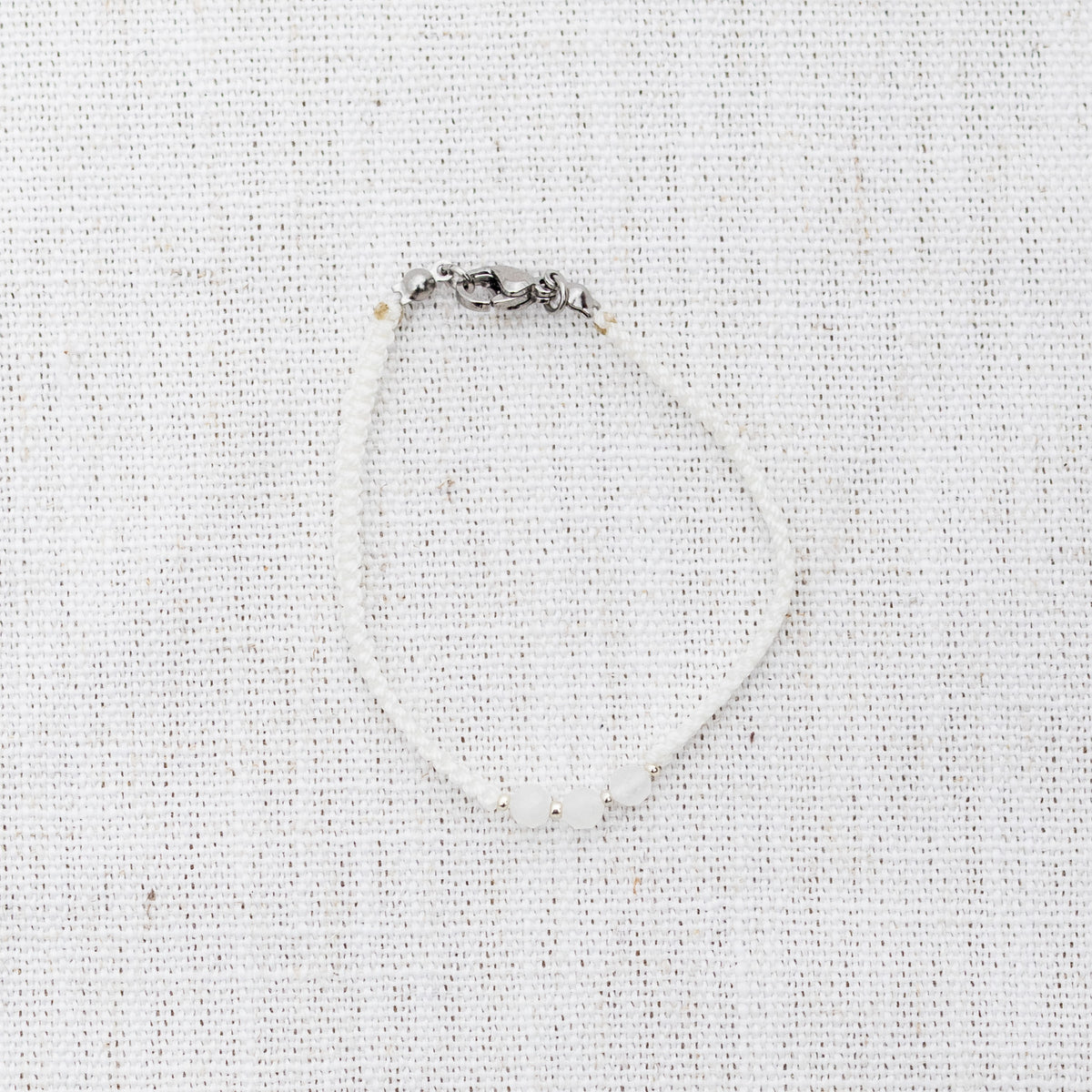 Intuitive Charms Selene's Guard Moonstone Braided natural Crystal beaded custom Bracelet in silver and white cord and clasp on a light fabric background