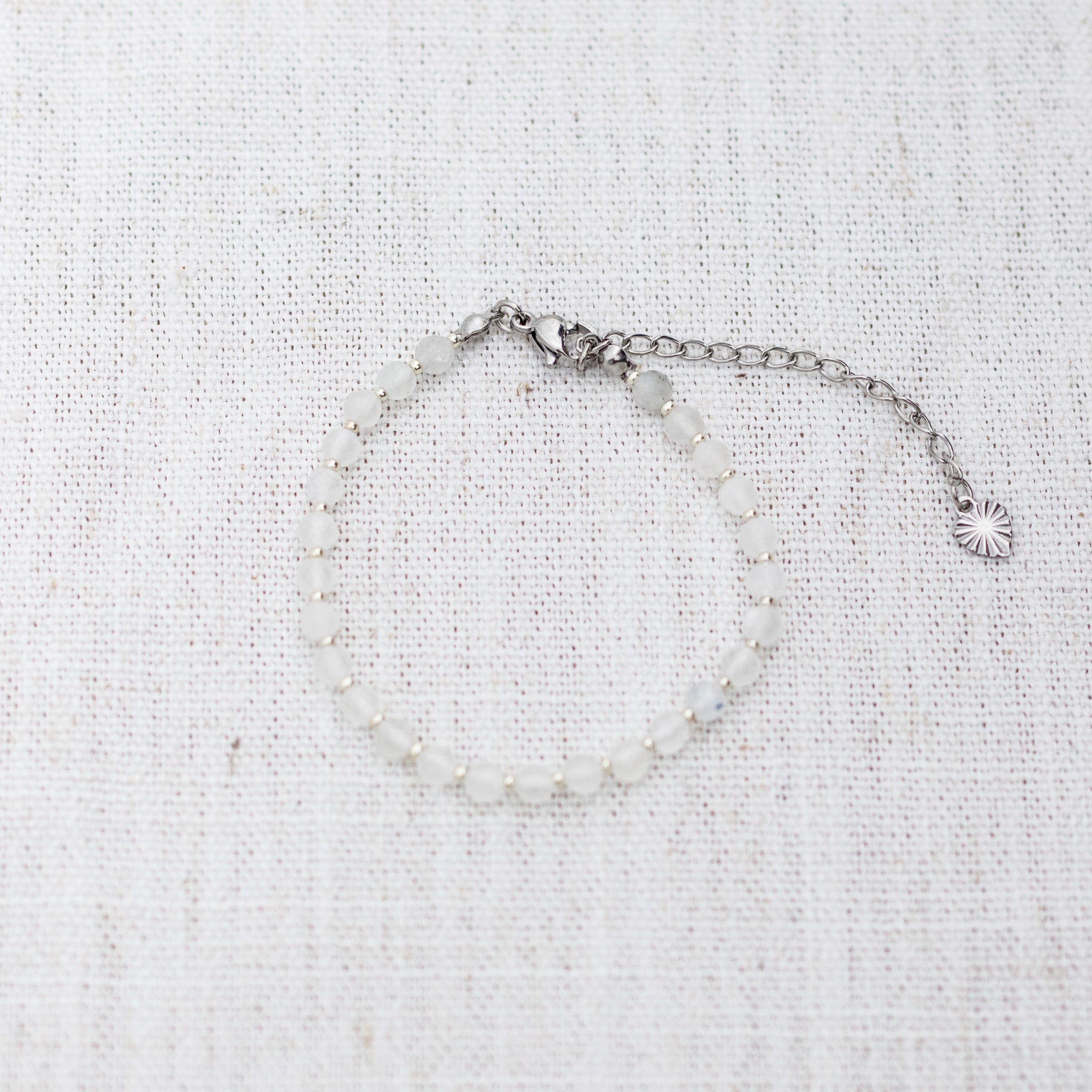 Intuitive Charms Selene's Glow Moonstone Braided natural Crystal beaded custom Bracelet in silver and white cord and clasp extension on a light fabric background