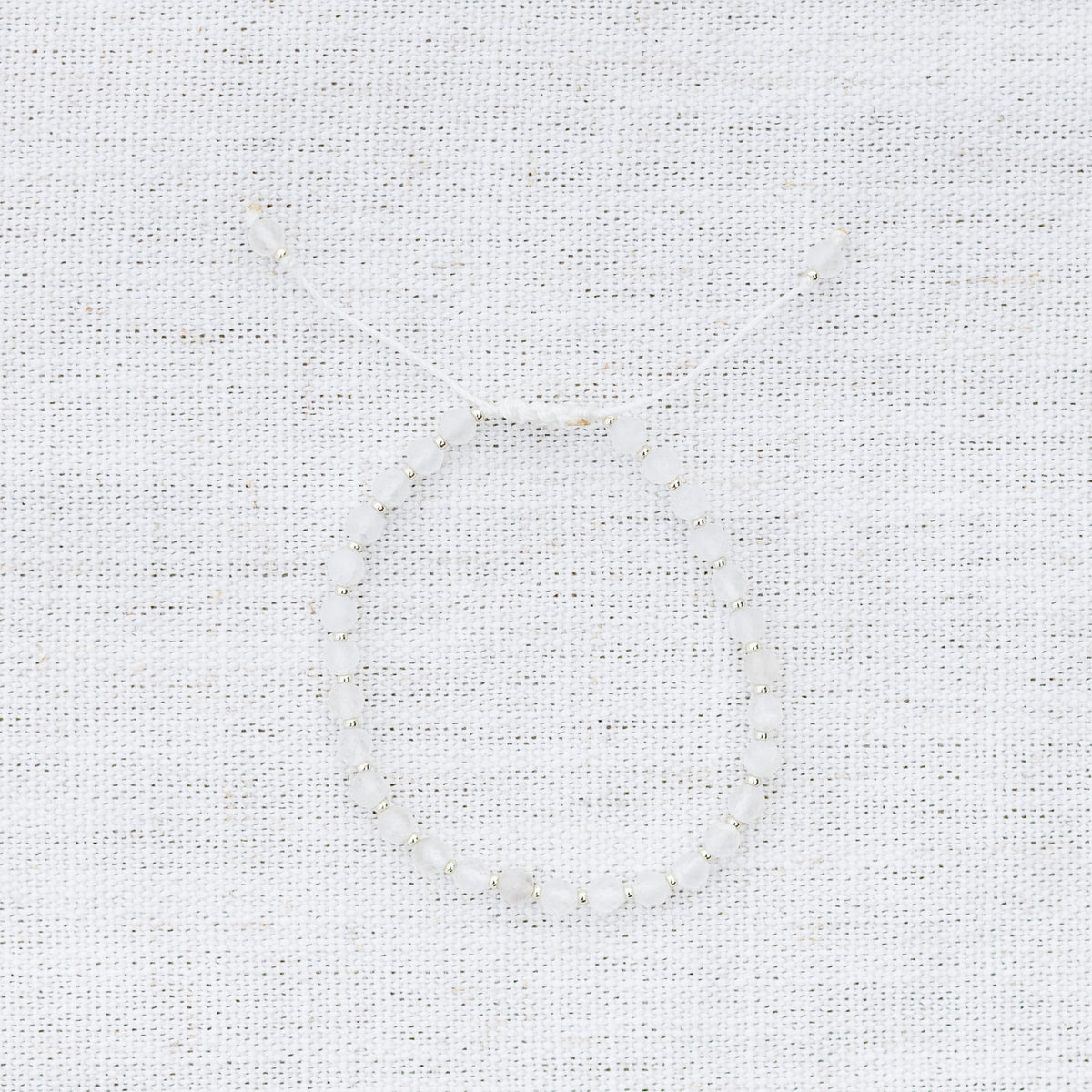 Intuitive Charms Selene's Glow Moonstone Braided natural Crystal beaded custom Bracelet in silver and white cord on a light fabric background