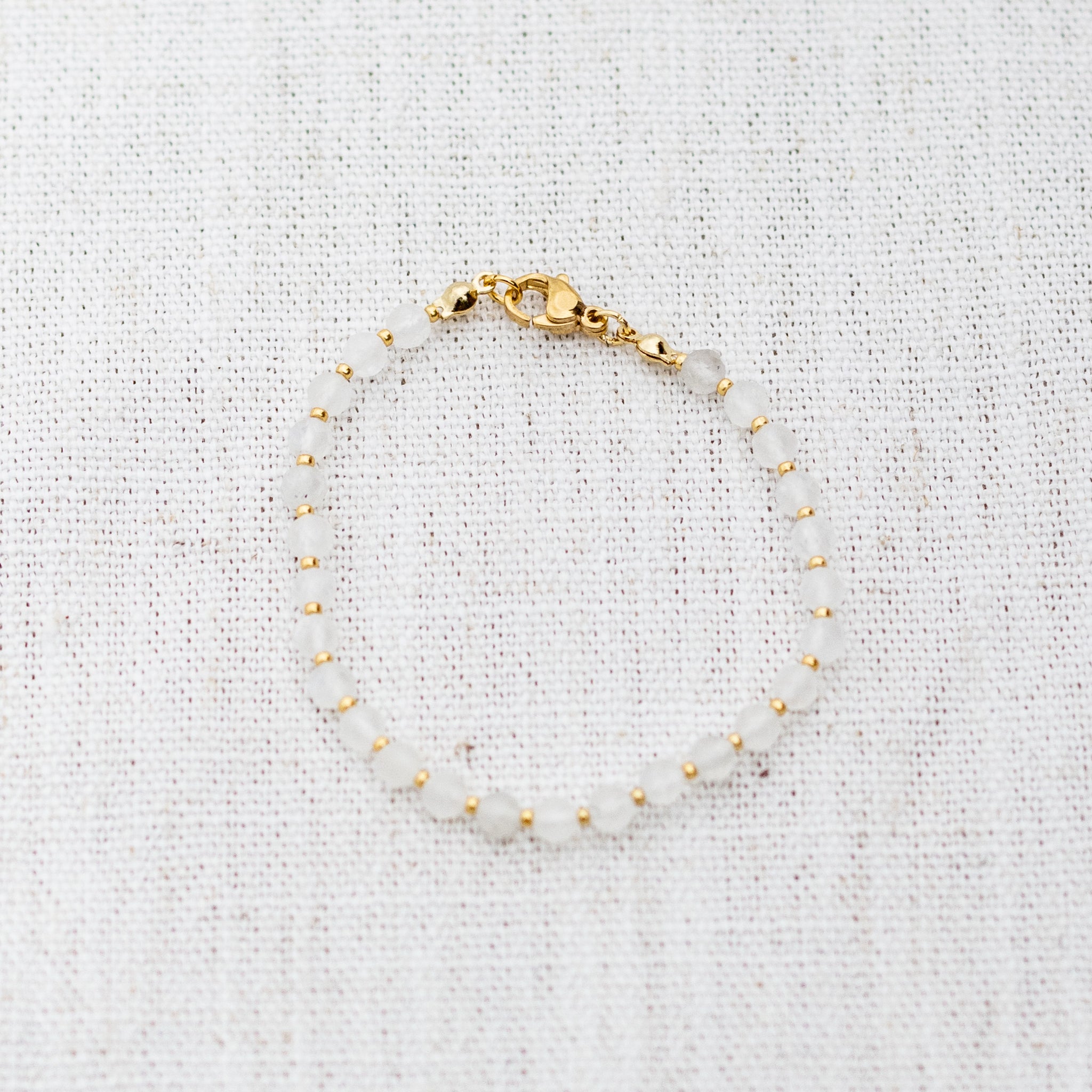 Intuitive Charms Selene's Glow Moonstone Braided natural Crystal beaded custom Bracelet in gold and white cord and clasp on a light fabric background
