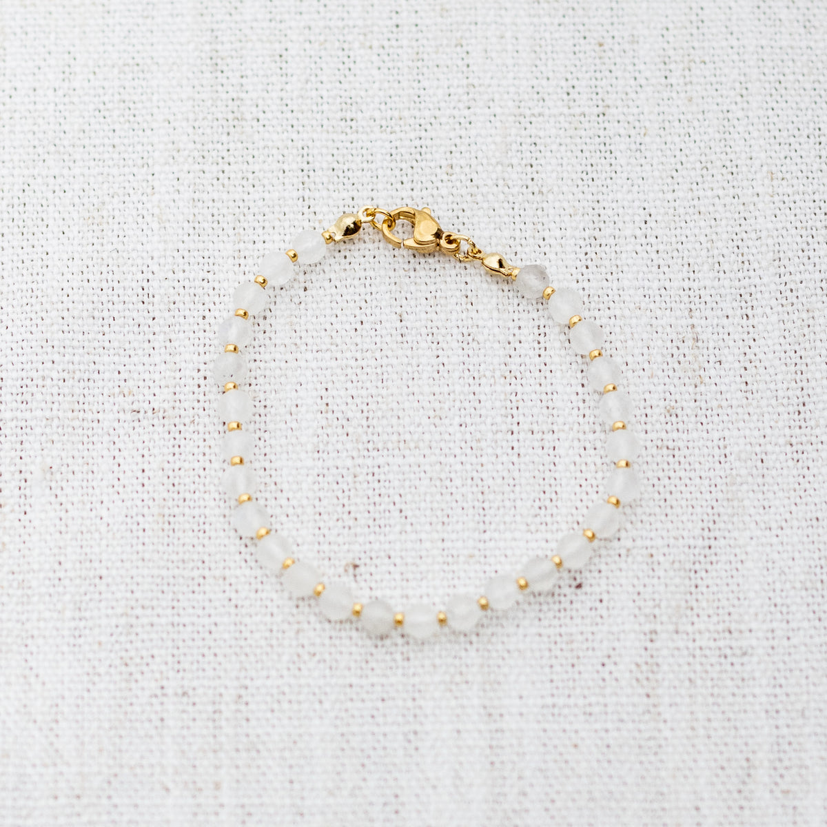 Intuitive Charms Selene's Glow Moonstone Braided natural Crystal beaded custom Bracelet in gold and white cord and clasp on a light fabric background