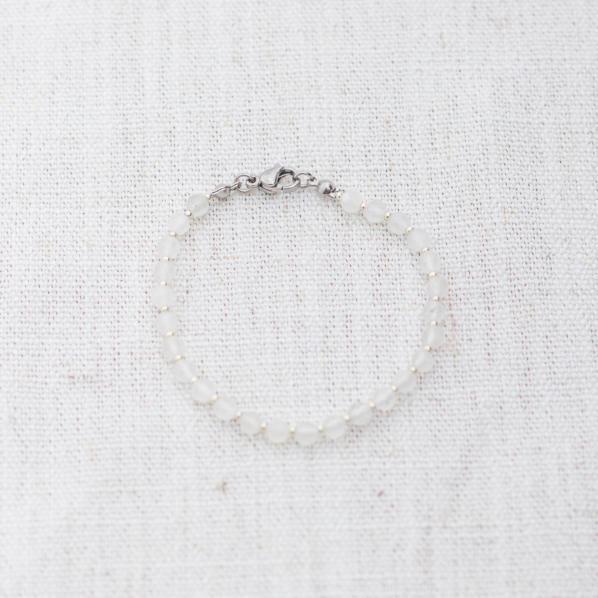 Intuitive Charms Selene's Glow Moonstone Braided natural Crystal beaded custom Bracelet in silver and white cord and clasp on a light fabric background