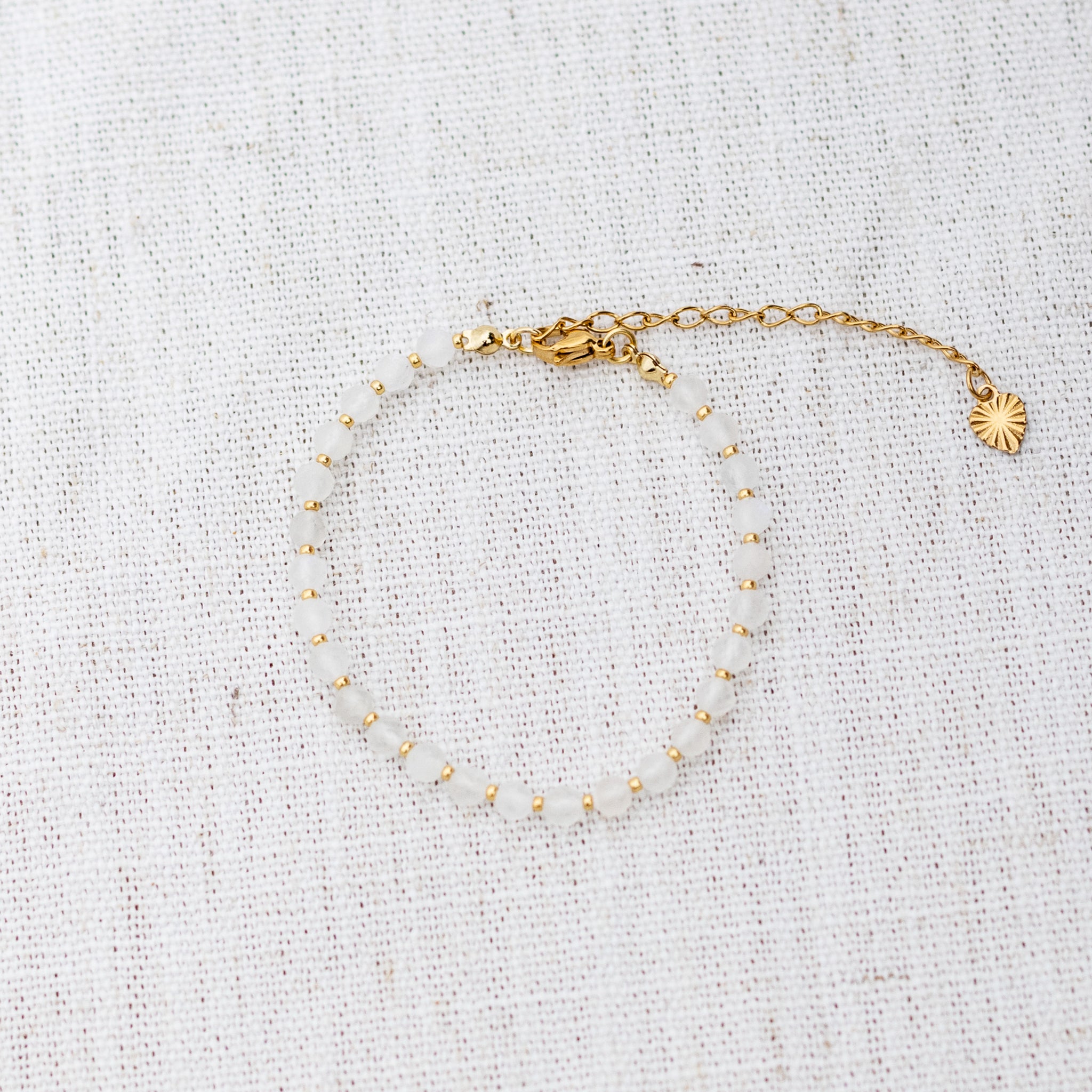 Intuitive Charms Selene's Glow Moonstone Braided natural Crystal beaded custom Bracelet in gold and white cord and clasp extension on a light fabric background