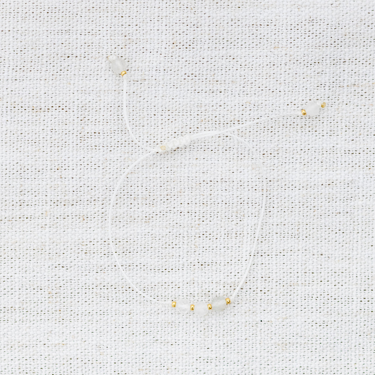 Intuitive Charms Selene's Mist Moonstone Braided natural Crystal beaded custom Bracelet in gold and white cord on a light fabric background