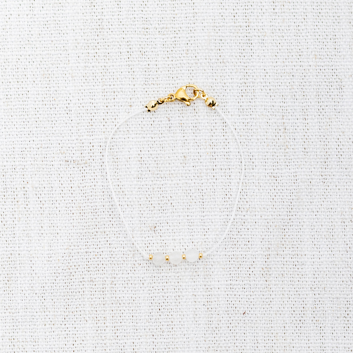 Intuitive Charms Selene's Mist Moonstone Braided natural Crystal beaded custom Bracelet in gold and white cord and clasp on a light fabric background
