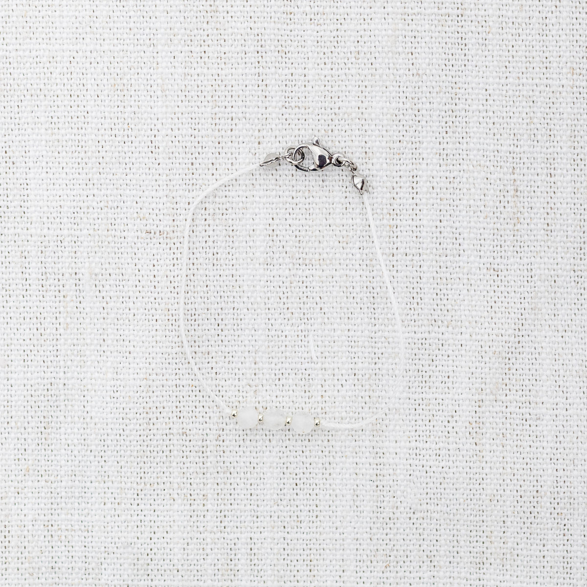 Intuitive Charms Selene's Mist Moonstone Braided natural Crystal beaded custom Bracelet in silver and white cord and clasp on a light fabric background
