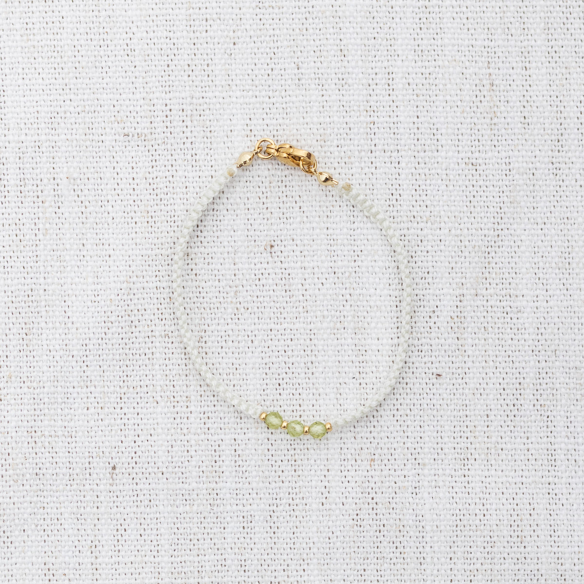 Intuitive Charms Nerina's Guard Peridot Braided natural Crystal beaded custom Bracelet in gold and light mint cord and clasp on a light fabric background