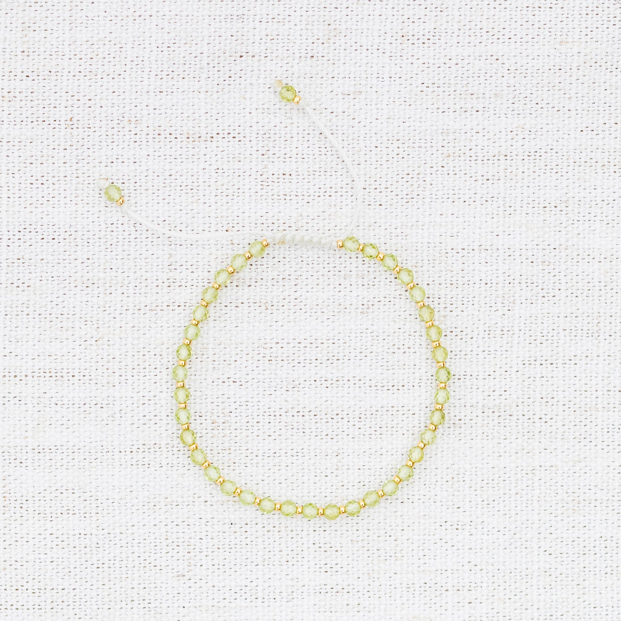 Intuitive Charms Nerina's Glow Peridot Braided natural Crystal beaded custom Bracelet in gold and light mint cord on a light fabric background