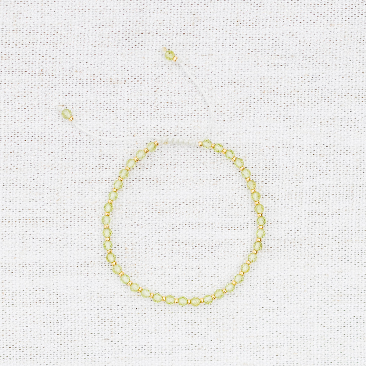 Intuitive Charms Nerina's Glow Peridot Braided natural Crystal beaded custom Bracelet in gold and light mint cord on a light fabric background