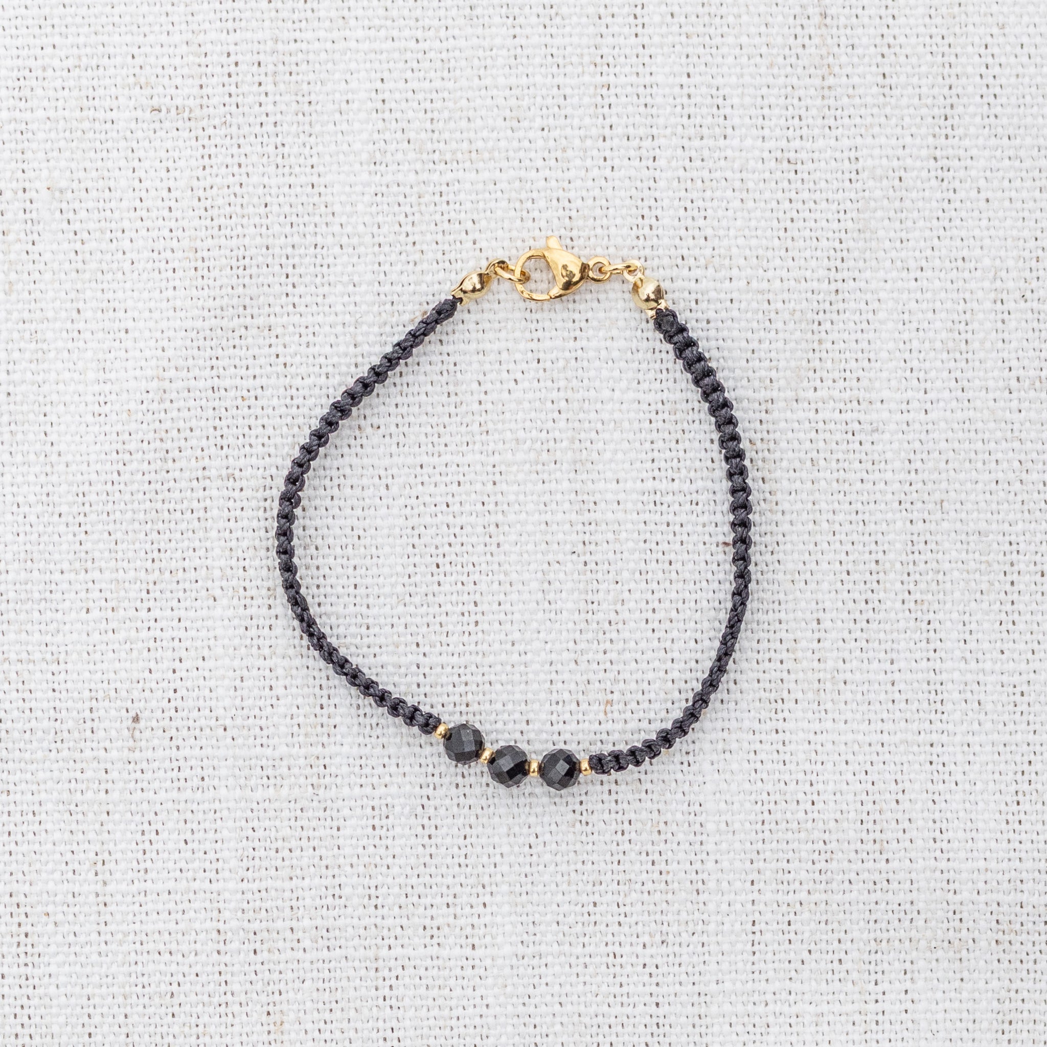 Intuitive Charms Ceto's Guard Black tourmaline Braided natural Crystal beaded custom Bracelet in gold and black cord and clasp on a light fabric background