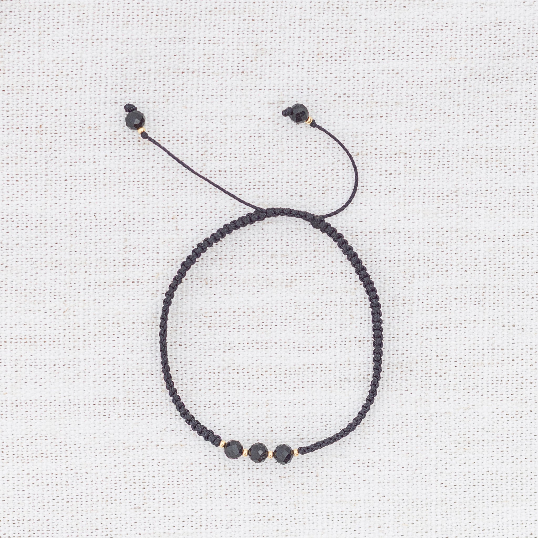 Intuitive Charms Ceto's Guard Black tourmaline Braided natural Crystal beaded custom Bracelet in gold and black cord on a light fabric background