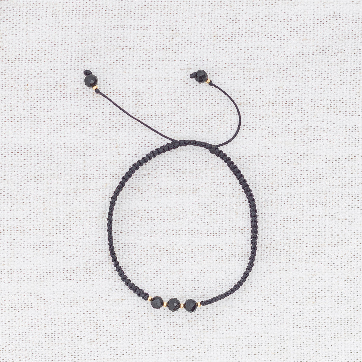 Intuitive Charms Ceto's Guard Black tourmaline Braided natural Crystal beaded custom Bracelet in gold and black cord on a light fabric background