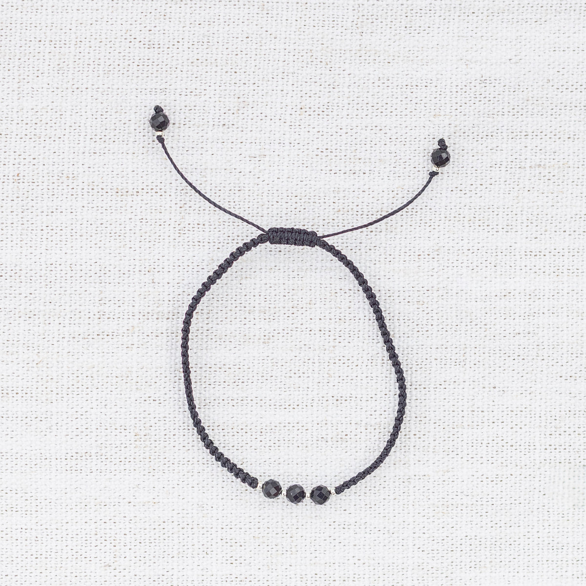 Intuitive Charms Ceto's Guard Black tourmaline Braided natural Crystal beaded custom Bracelet in silver and black cord on a light fabric background