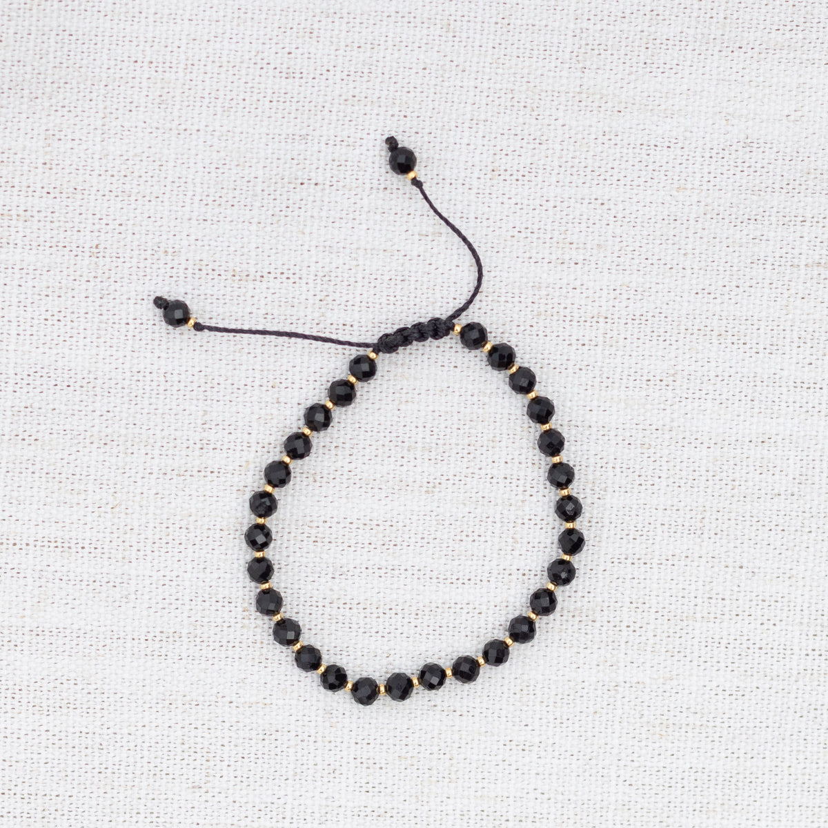 Intuitive Charms Ceto's Glow Apatite Braided natural Crystal beaded custom Bracelet in gold and black cord on a light fabric background