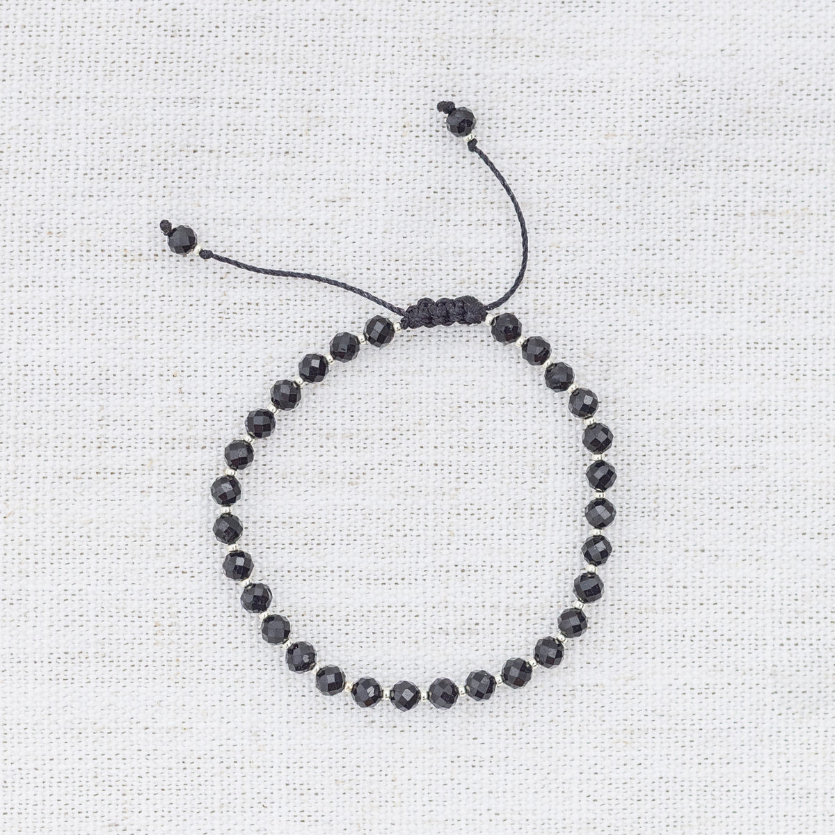 Intuitive Charms Ceto's Glow Apatite Braided natural Crystal beaded custom Bracelet in silver and black cord on a light fabric background
