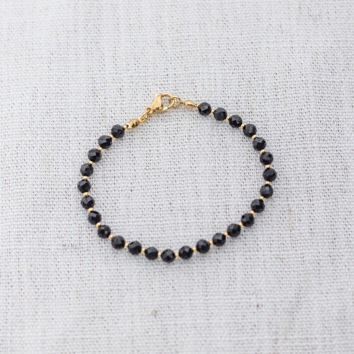 Intuitive Charms Ceto's Glow Apatite Braided natural Crystal beaded custom Bracelet in gold and black cord and clasp on a light fabric background