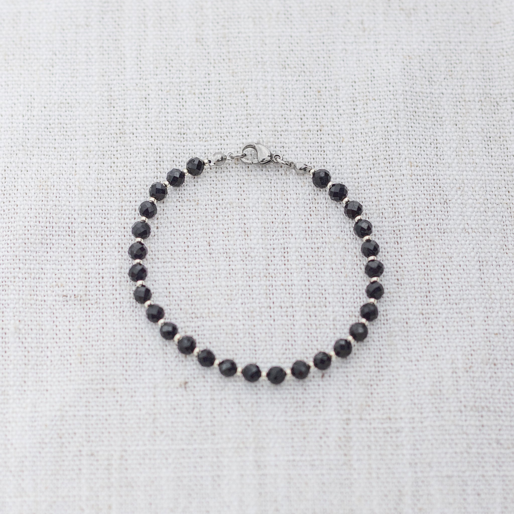 Intuitive Charms Ceto's Glow Apatite Braided natural Crystal beaded custom Bracelet in silver and black cord and clasp on a light fabric background