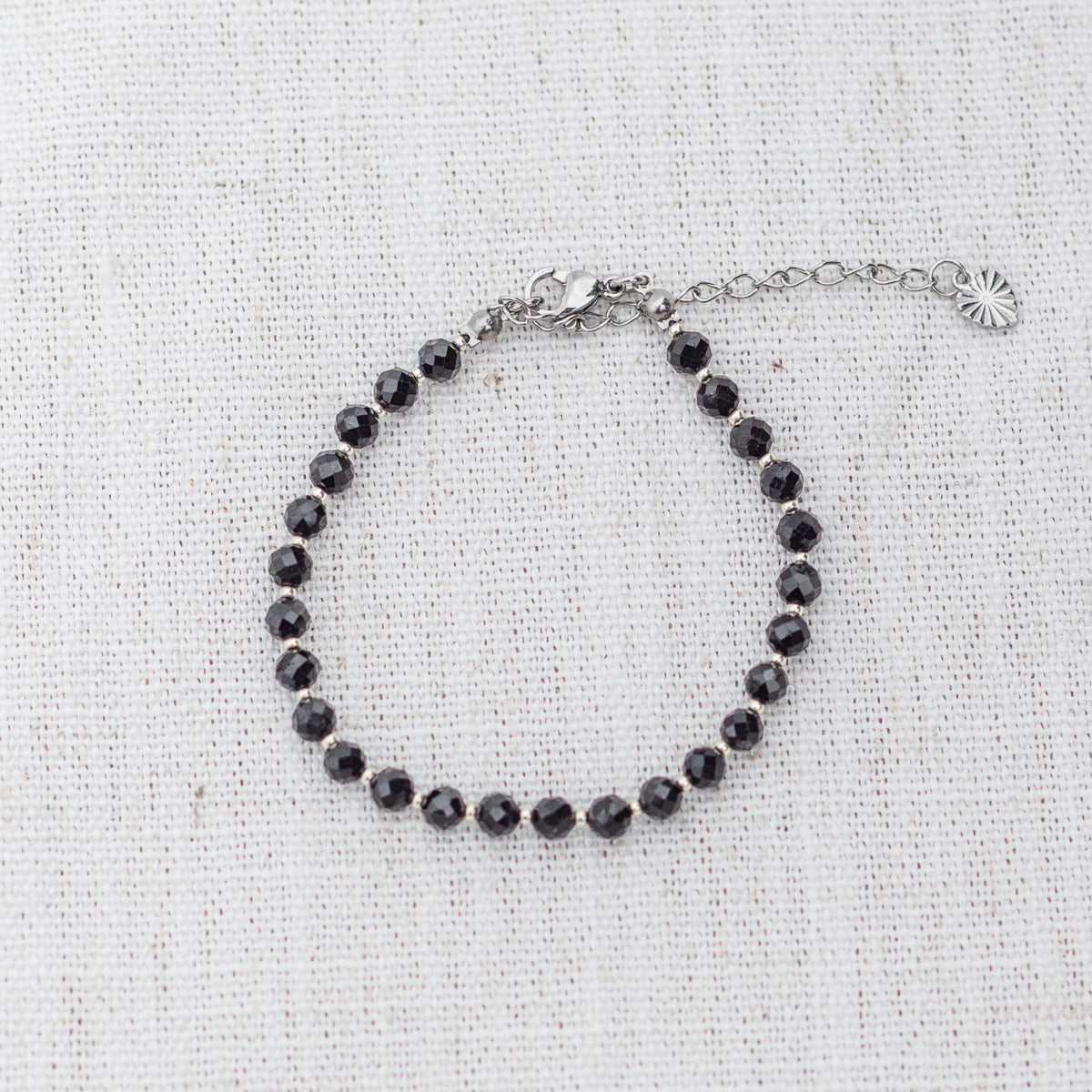 Intuitive Charms Ceto's Glow Apatite Braided natural Crystal beaded custom Bracelet in silver and black cord and clasp extension on a light fabric background