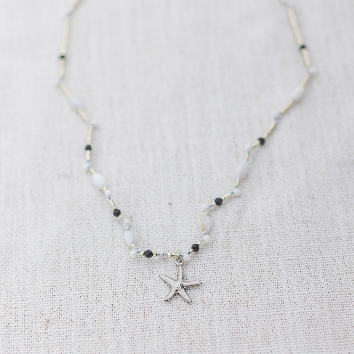 Intuitive Charms Ceto's Song Black tourmaline Braided natural Crystal beaded custom necklace in silver and black cord on a light fabric background